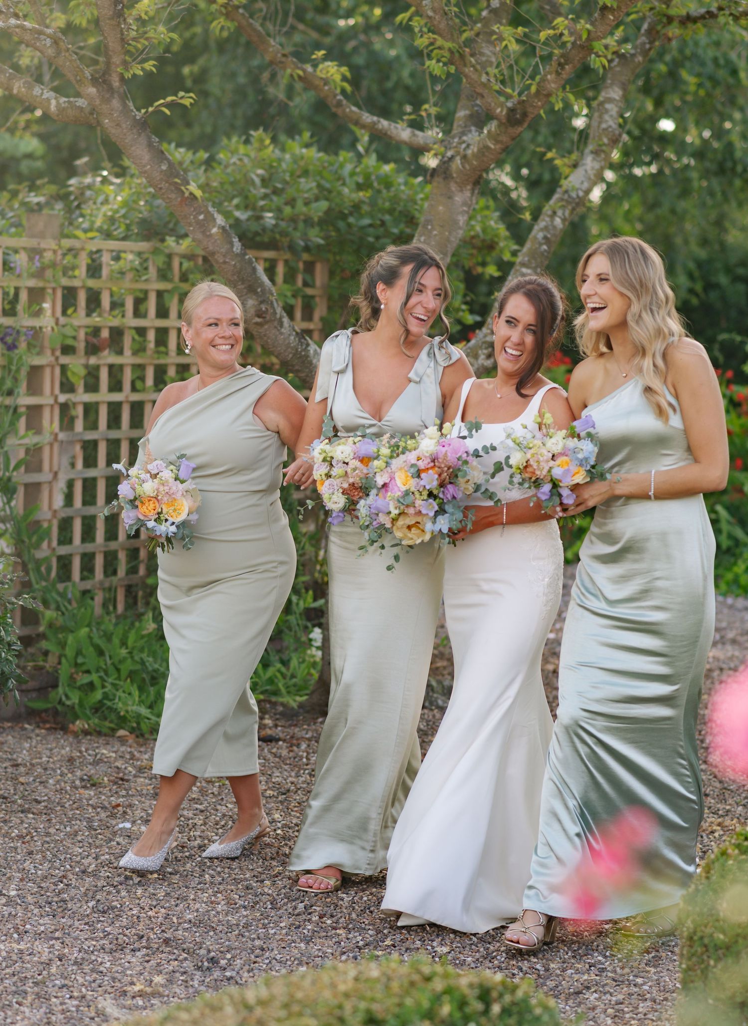 A group in silver dresses poses playfully in a garden setting with floral bouquets.