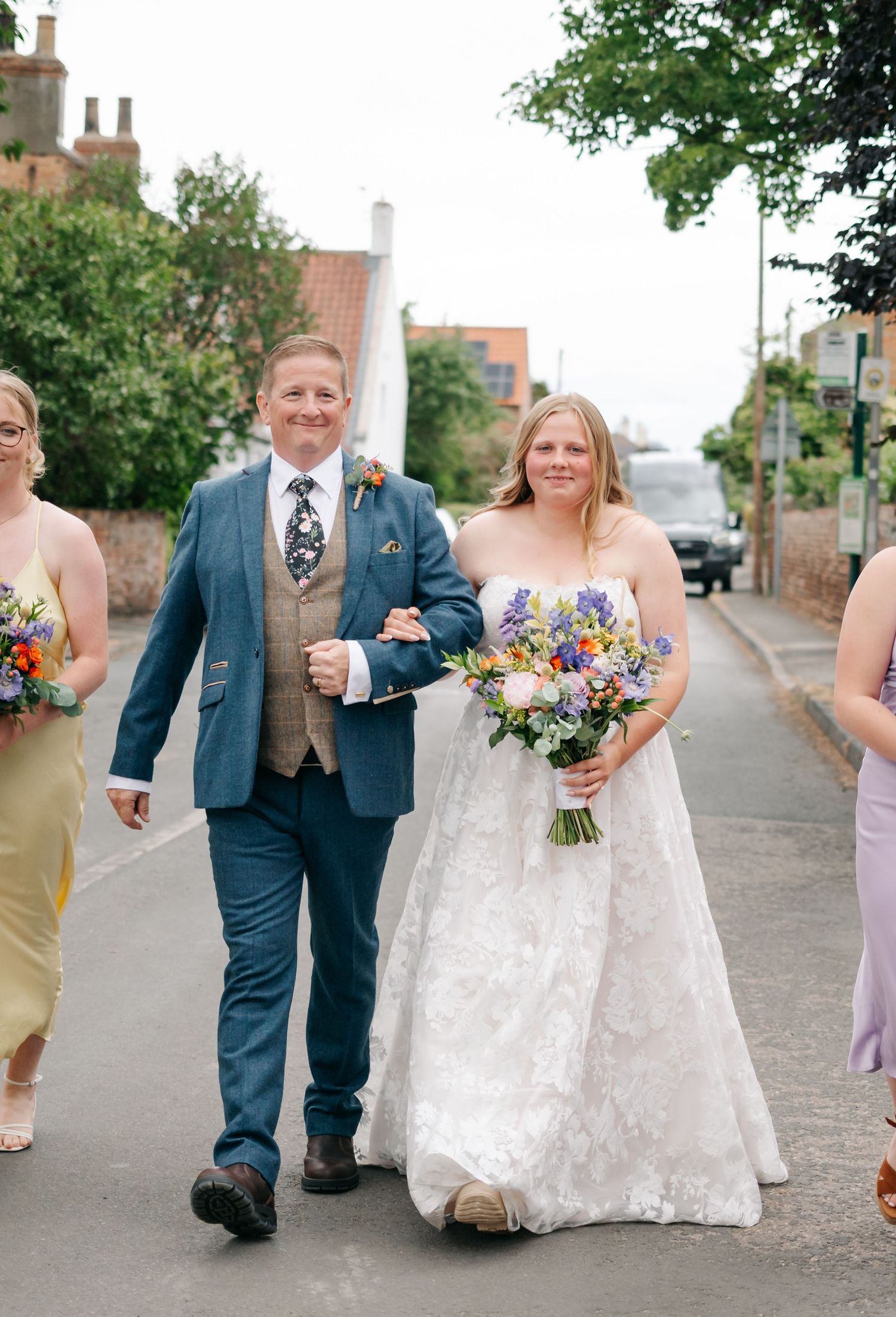 Wedding party walking down a cobblestone street with bride in white dress and purple bridesmaid dresses.