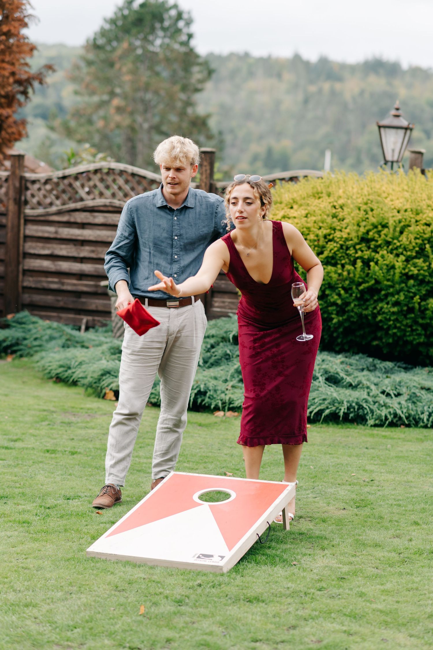 Wedding guests play cornhole on a manicured lawn during outdoor reception festivities.