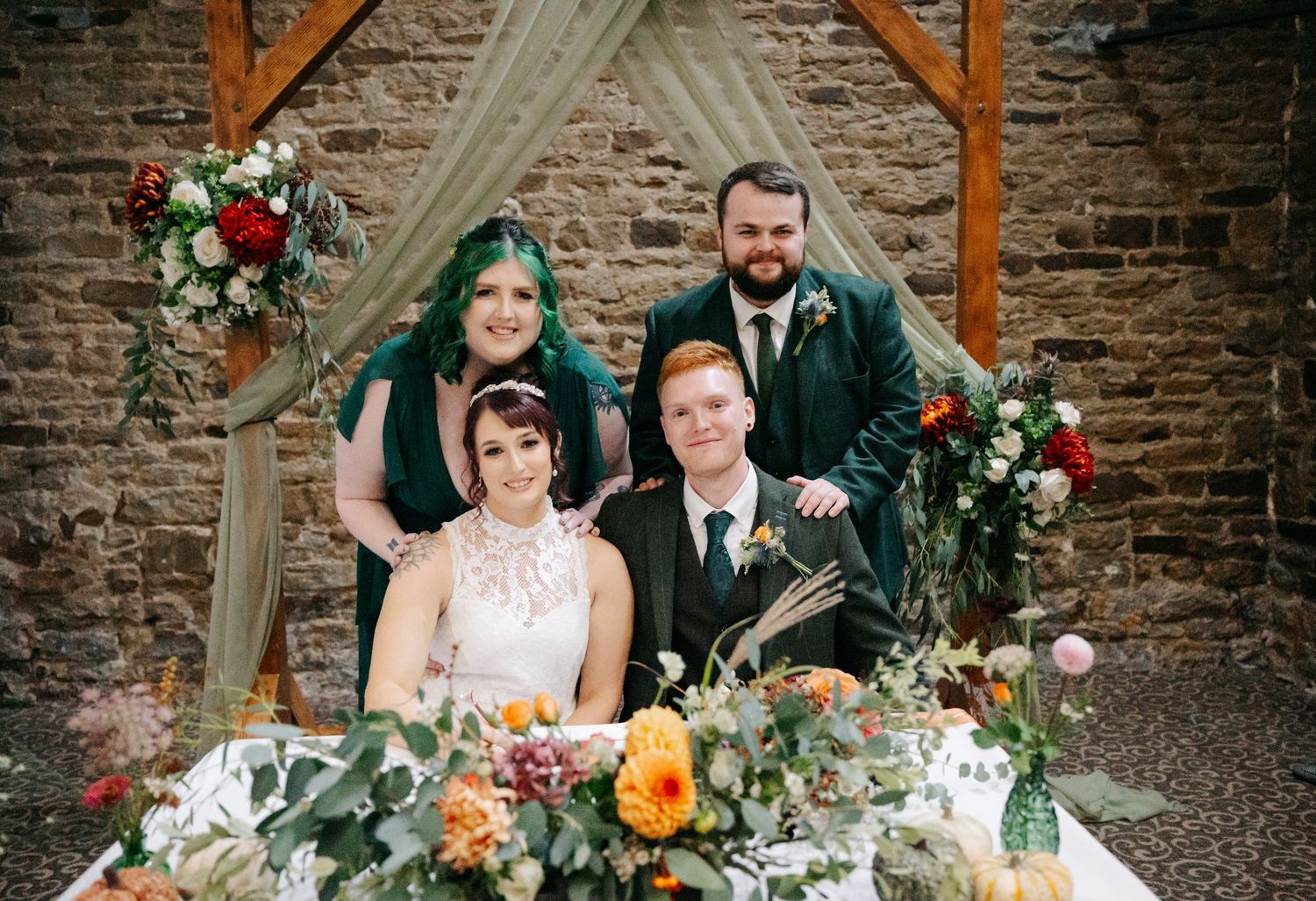 Rustic wedding ceremony with autumn floral arrangements and stone wall backdrop.