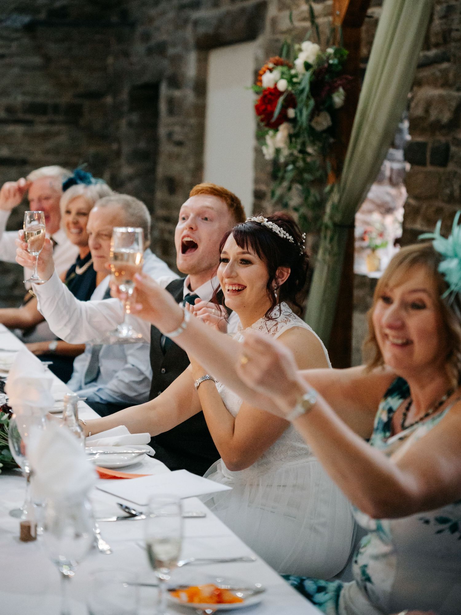 Wedding guests laugh and raise their glasses during a joyful toast at an elegant reception dinner.