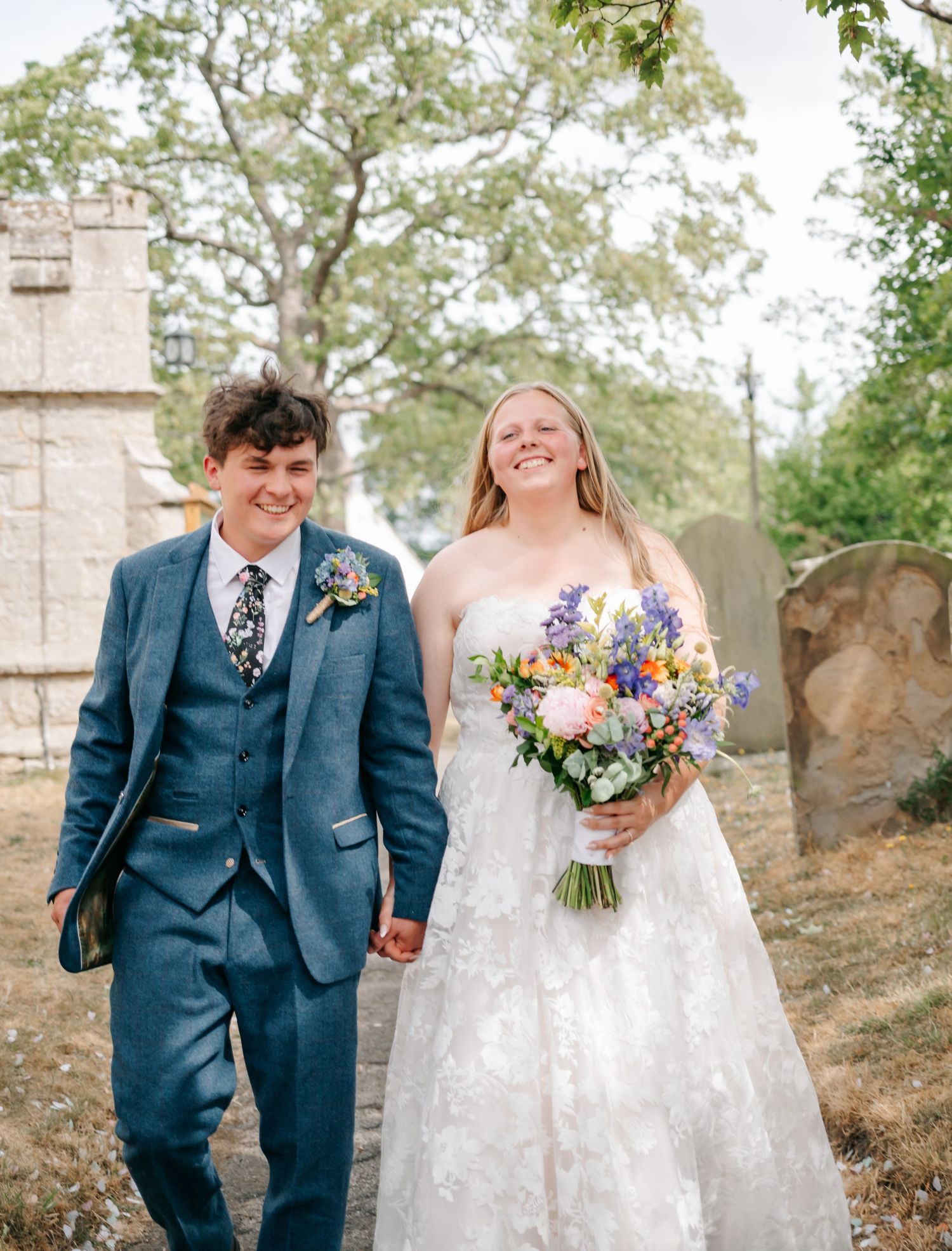 Newlyweds walking and laughing together on rustic outdoor grounds.