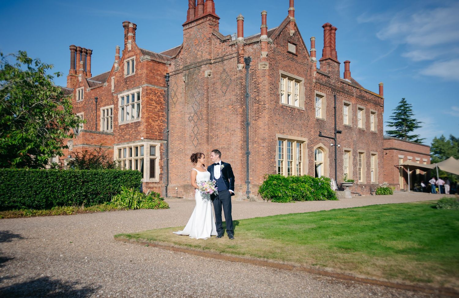 A panoramic view of a grand red brick manor house with ornate architectural details.