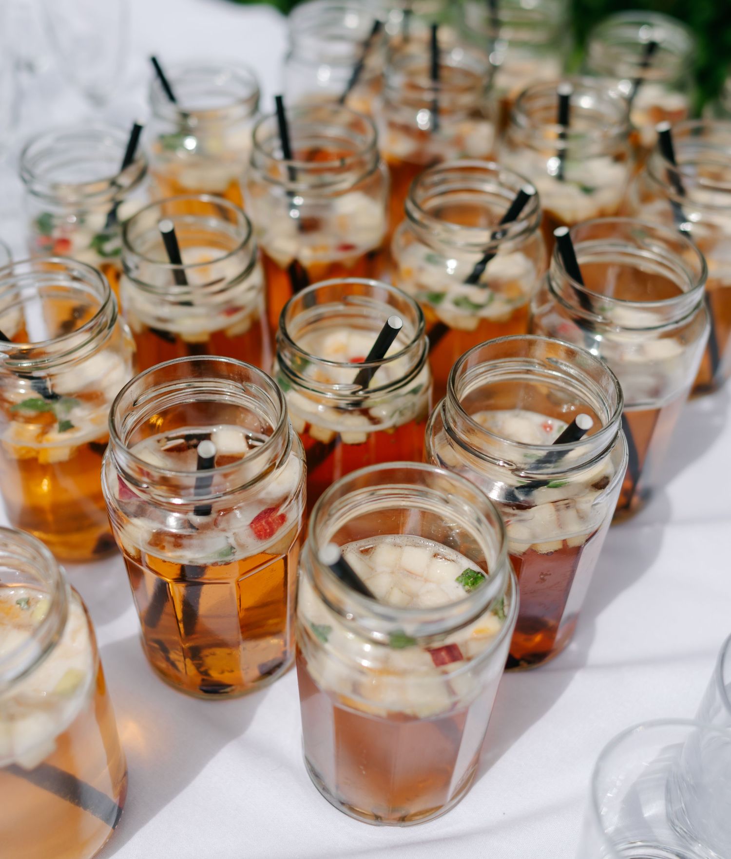 Mason jars filled with iced tea and straws lined up on a white tablecloth.
