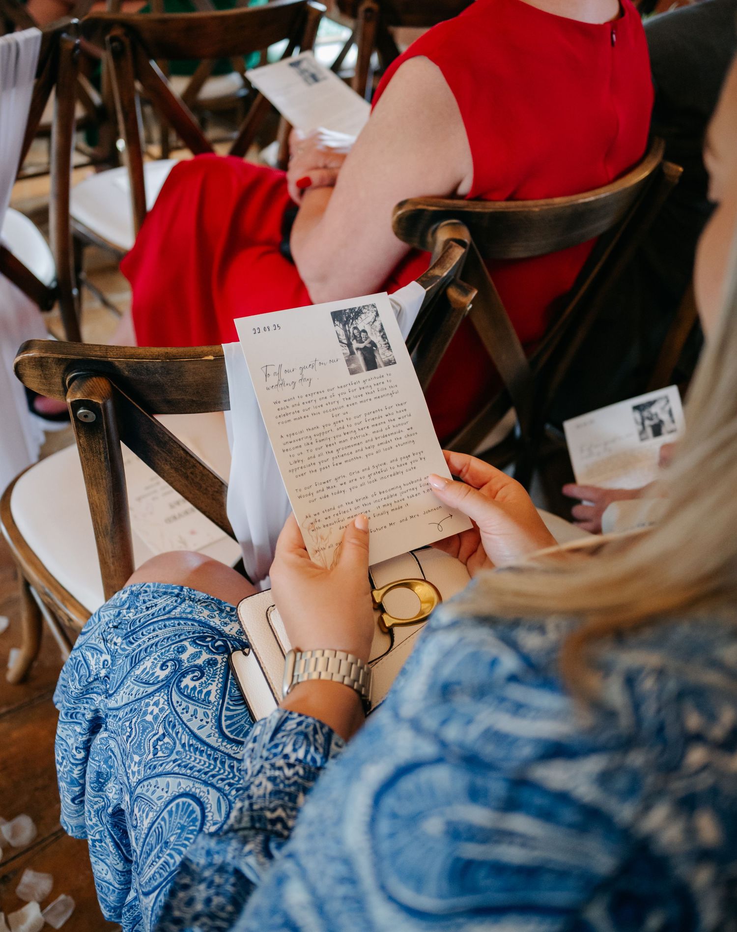 Wedding guests reading handwritten letters during ceremony while seated in wooden chairs.
