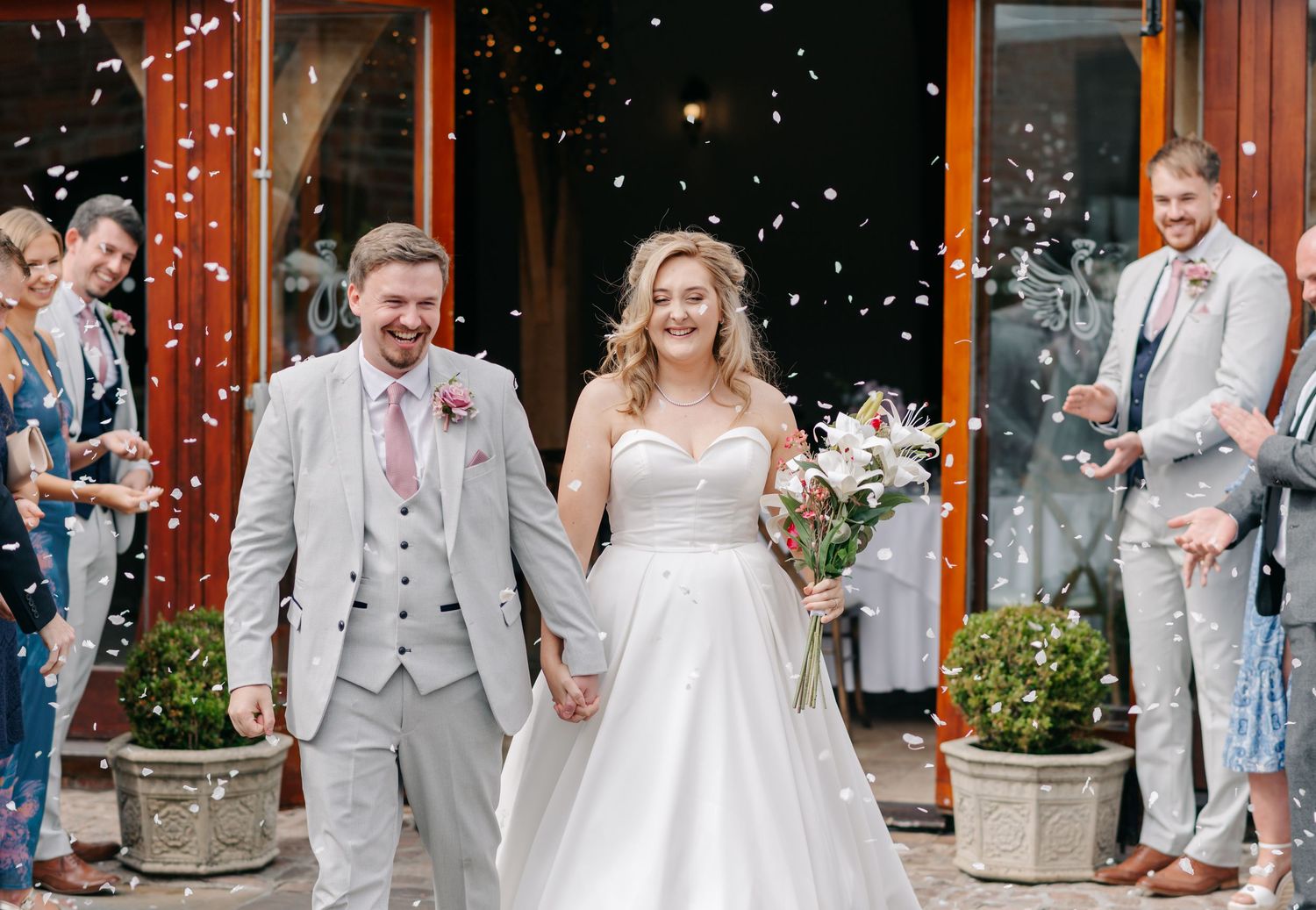 Wedding party celebrates with rice confetti toss outside a rustic venue.
