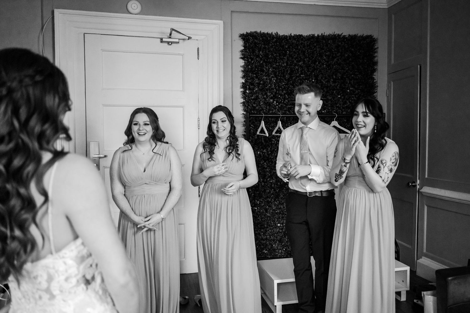 Wedding party members stand in a room with a black backdrop during preparation.