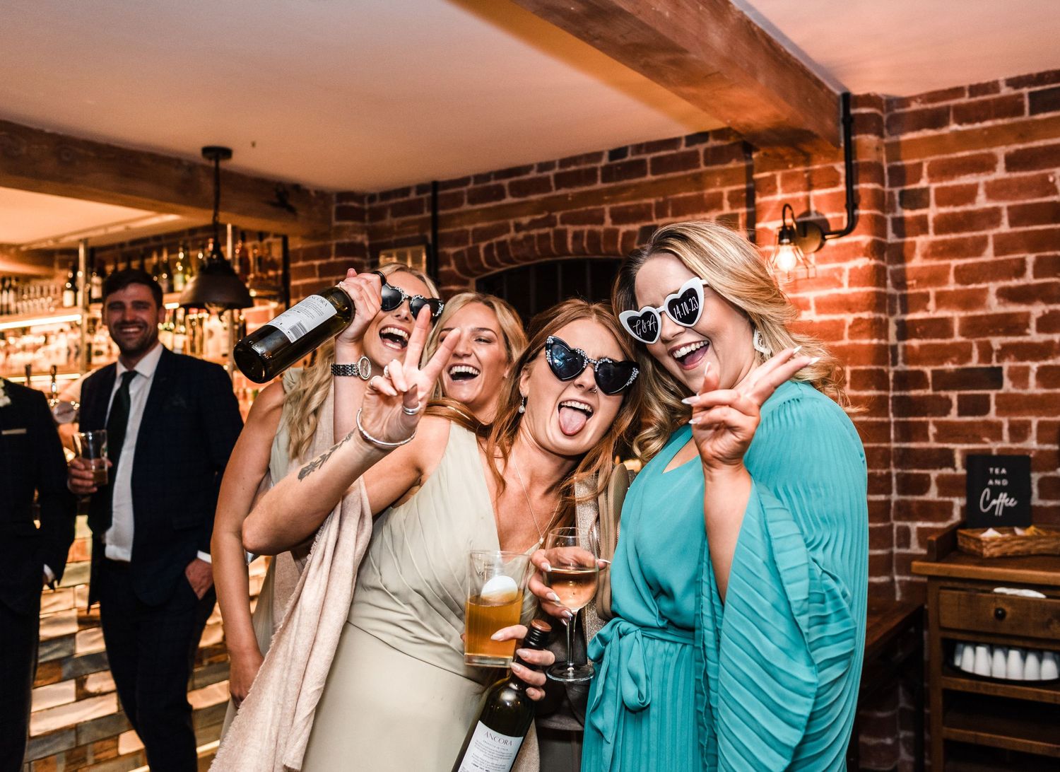 Wedding party guests enjoying drinks and wearing sunglasses at a rustic brick venue reception.