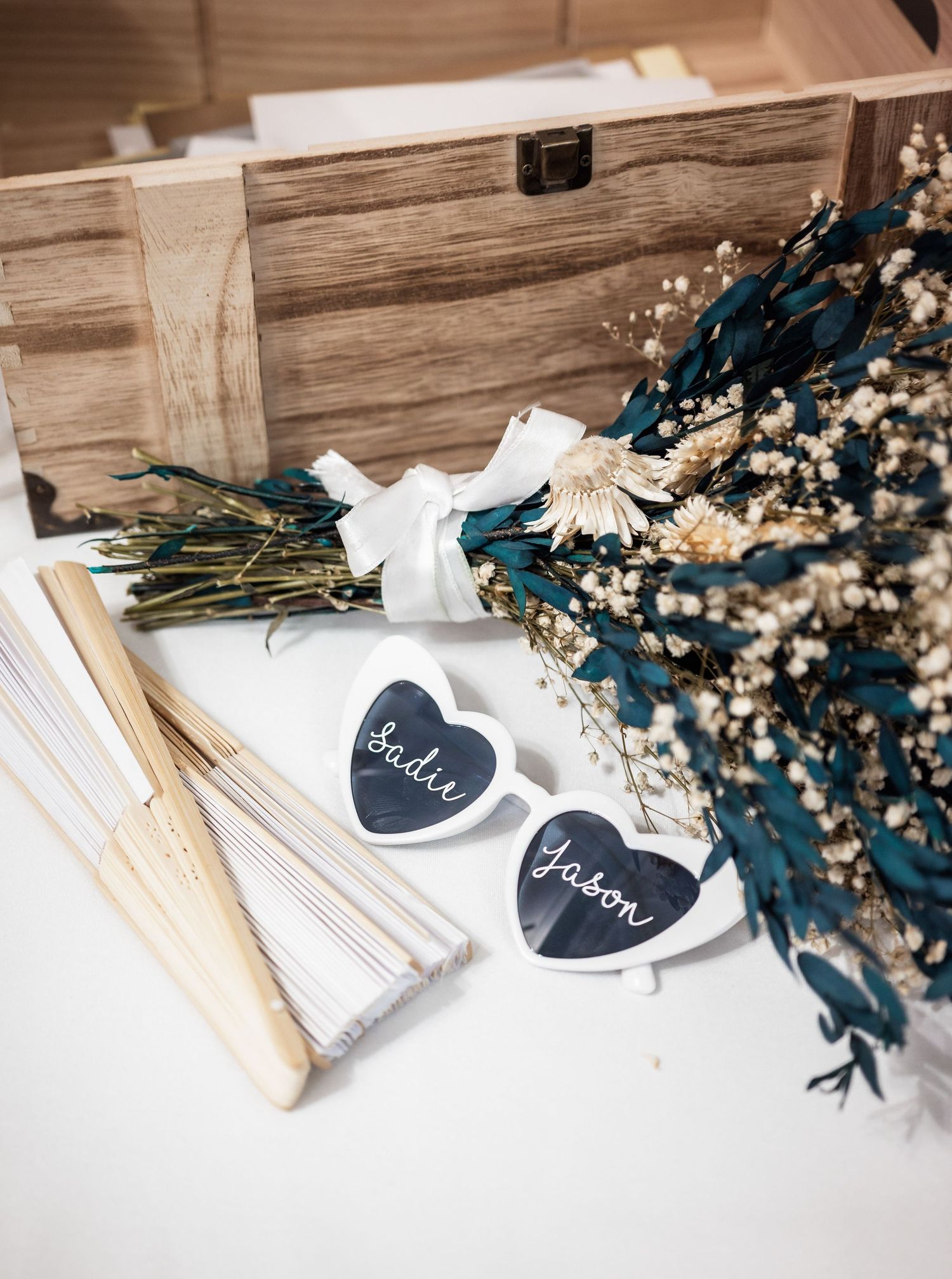 Wedding detail shot of dried blue florals and heart-shaped signs on wooden surface.