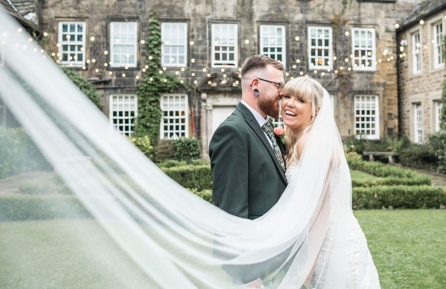 A romantic portrait with billowing veil against classic English manor architecture.