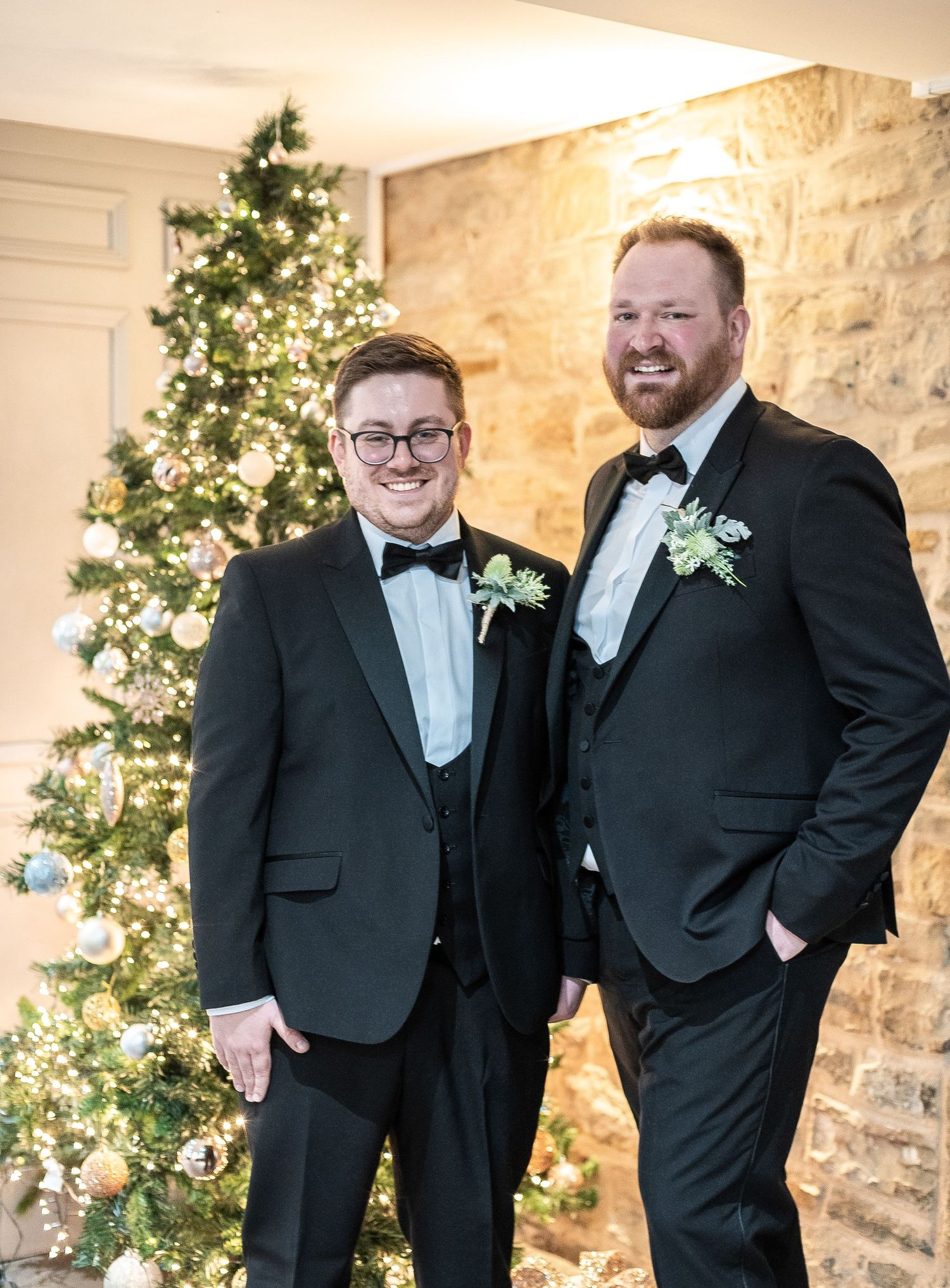 Wedding portrait in front of a decorated Christmas tree with stone wall backdrop.