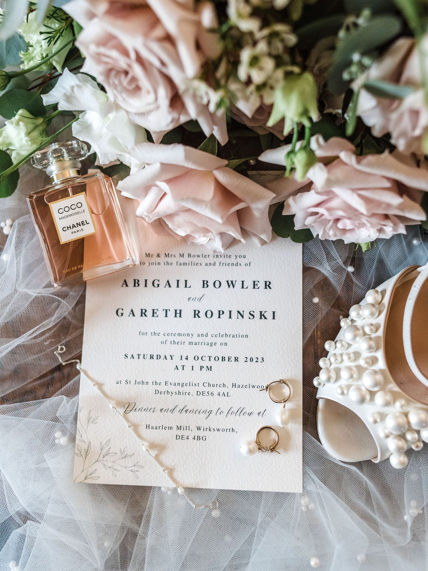 Wedding invitation with pink roses, perfume bottle and rings on delicate tulle fabric.