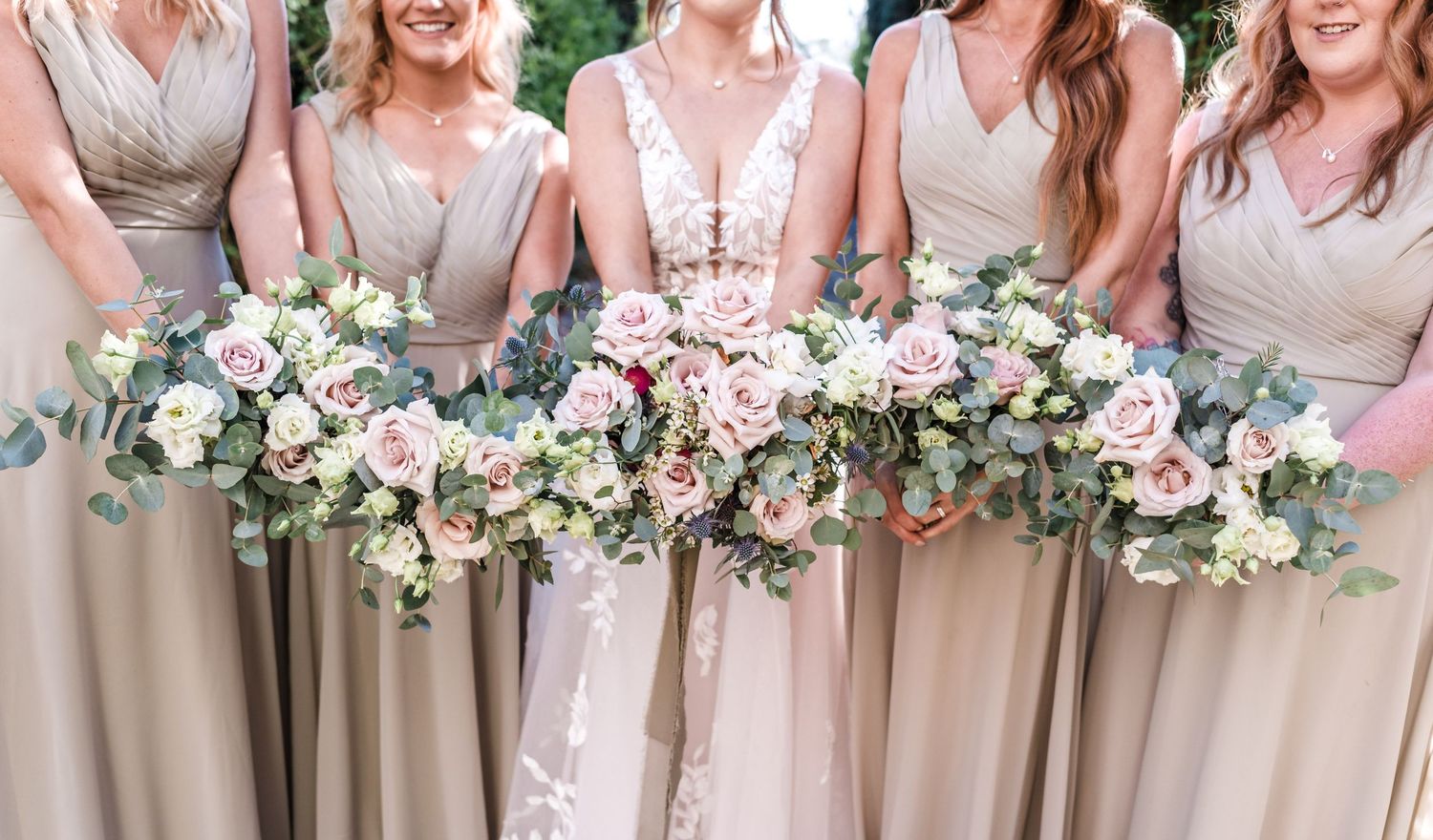 Elegant bridesmaids bouquets with pink roses and eucalyptus against blush dresses.