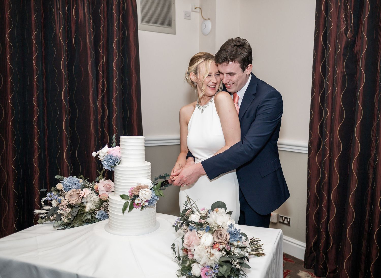 Newlyweds cut their elegant white wedding cake decorated with flowers.