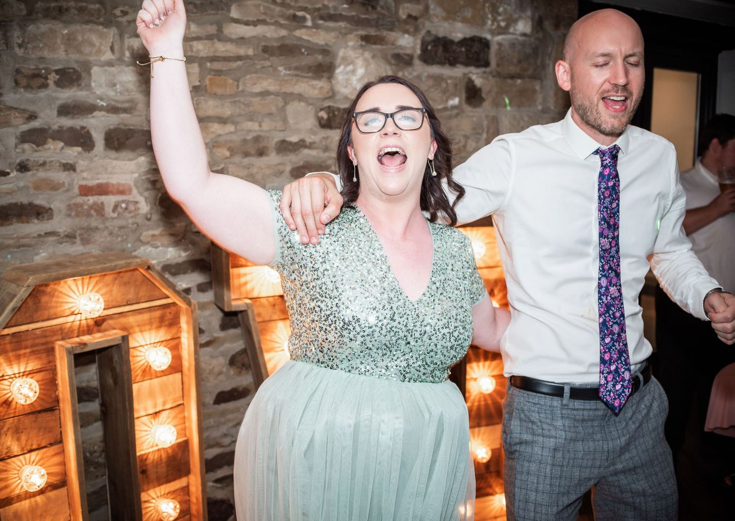 A speaker addresses wedding guests in a rustic venue with exposed wooden beams.