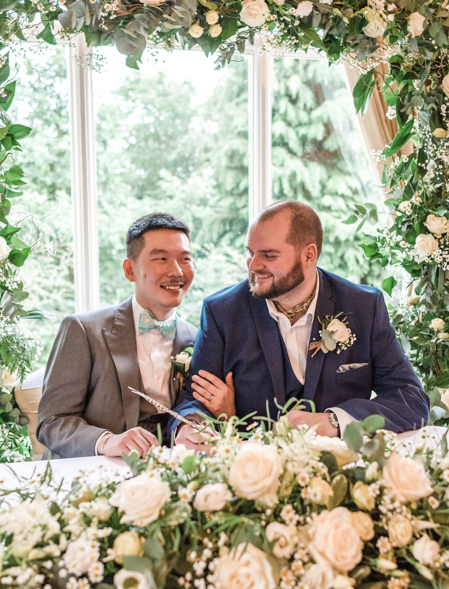 Two people sign documents at a flower-adorned table during their wedding ceremony.
