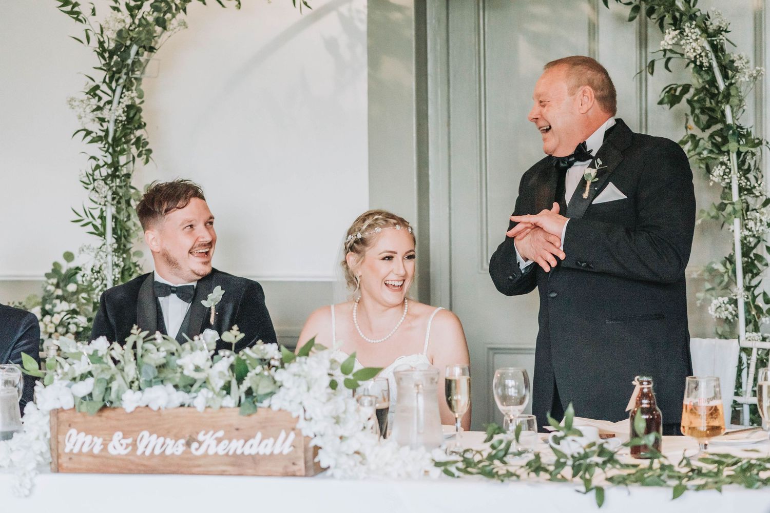 Wedding reception speech at head table with elegant greenery arch and Mr & Mrs sign.