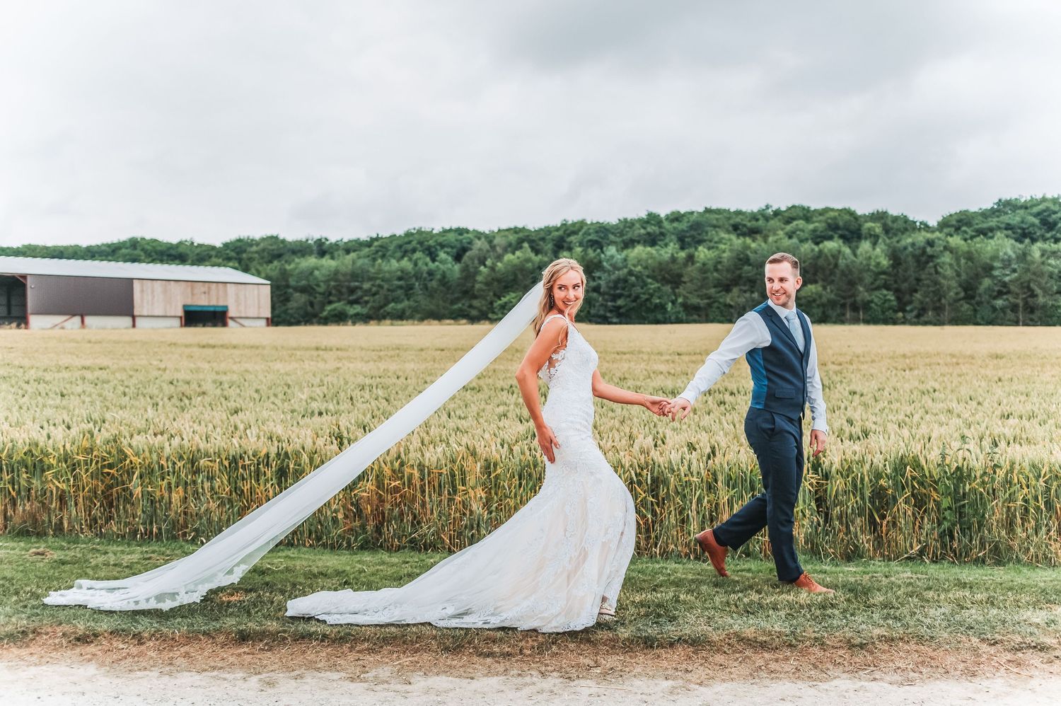 Couple walking in a wheat field with bride's veil flowing in the breeze.