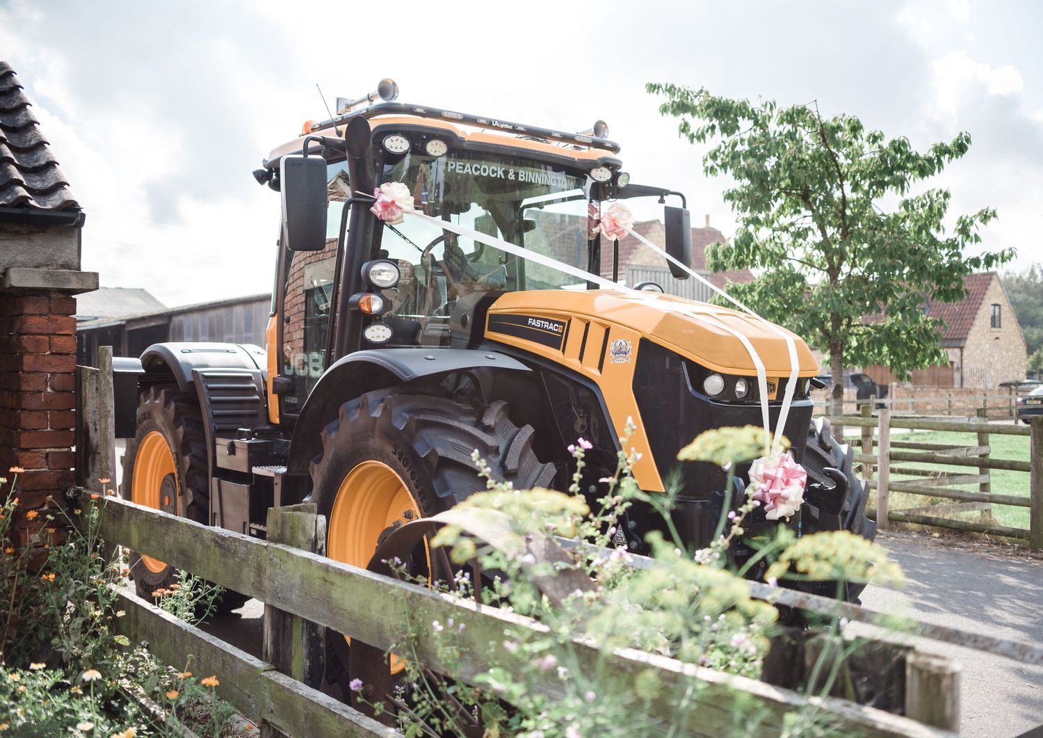 Yellow JCB tractor decorated with flowers parked outside rustic farm building.