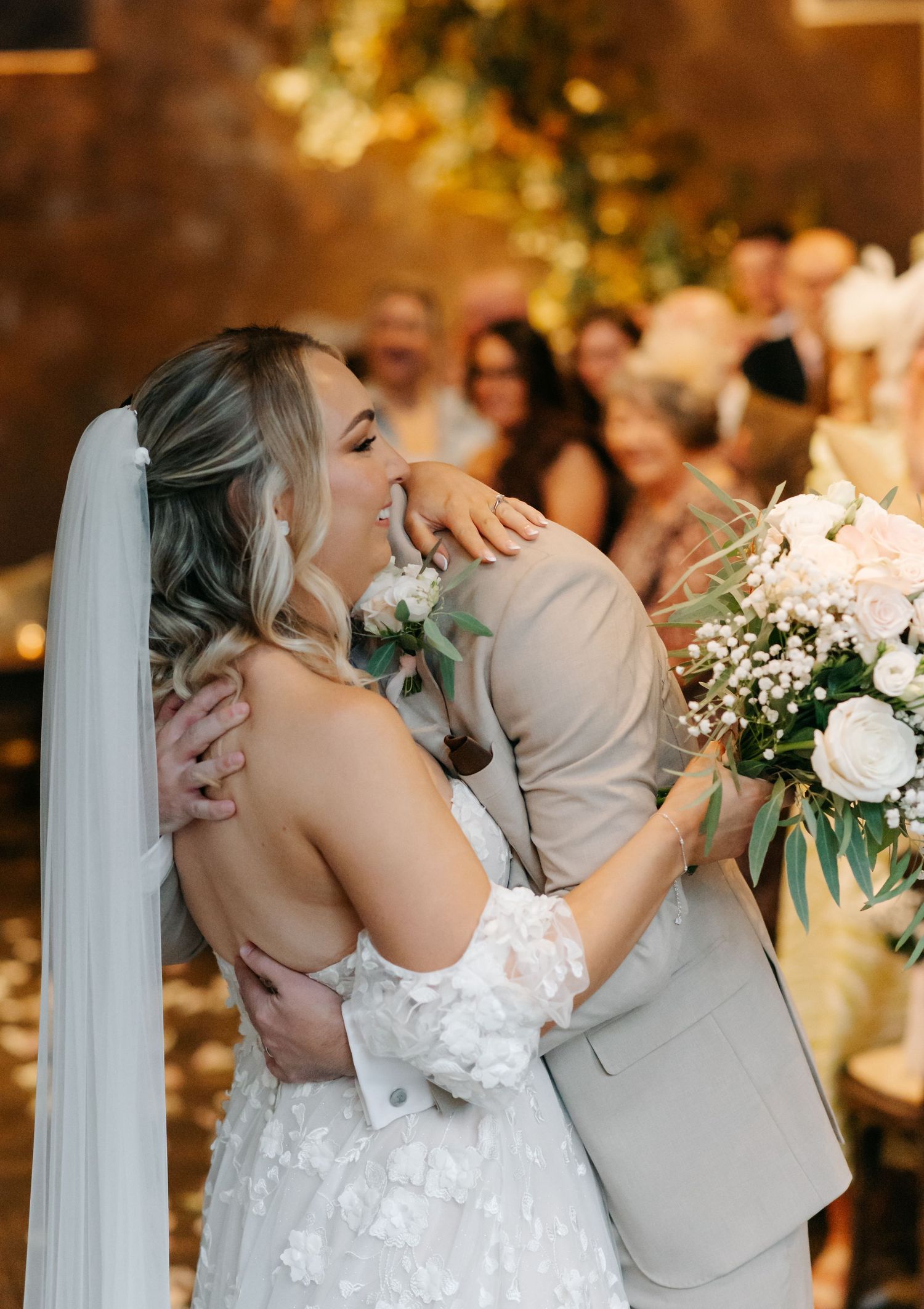 A joyful moment at a wedding reception as a couple embraces while surrounded by floral decorations and guests.