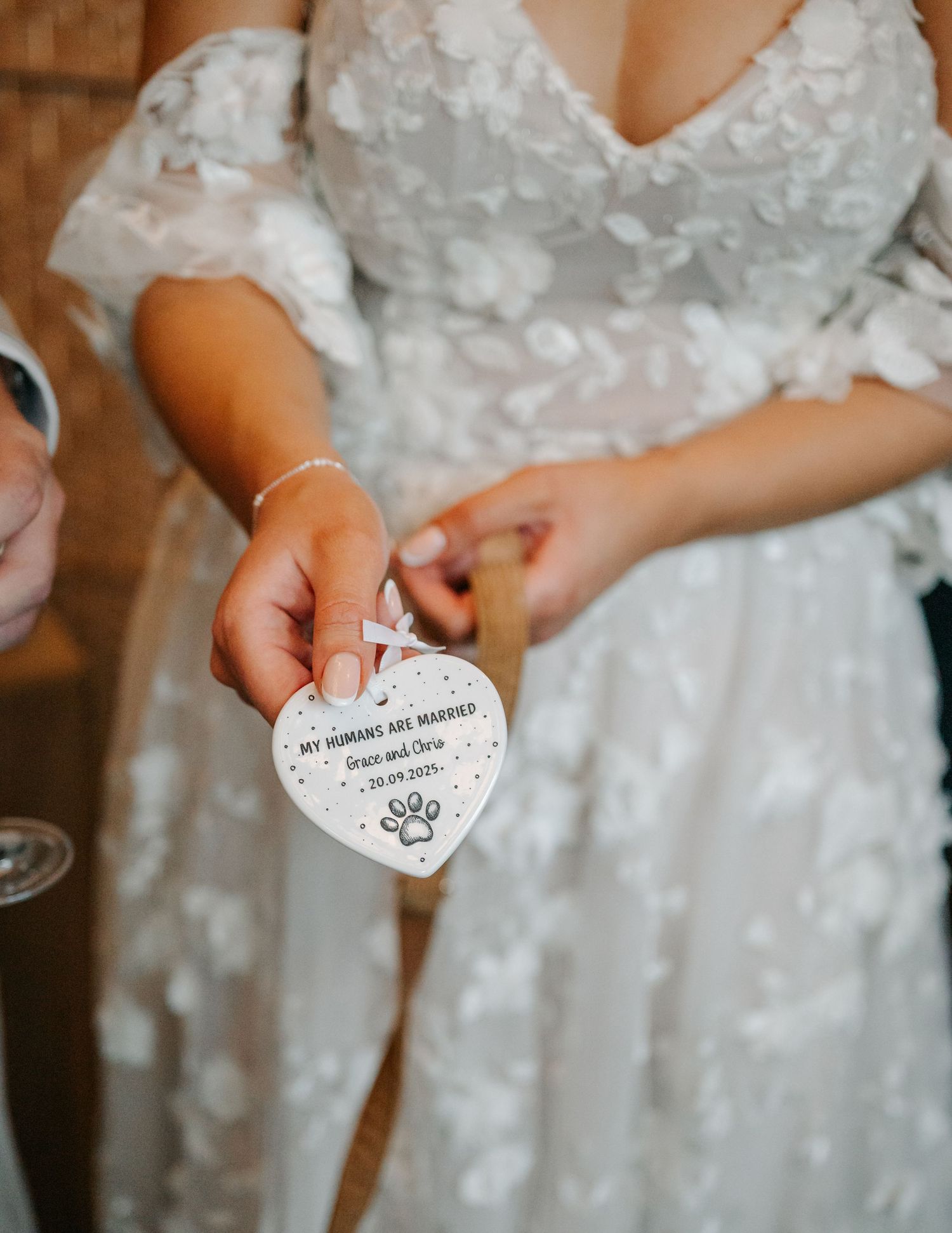 Close-up of bride's hands holding white decorative item against lace wedding dress.