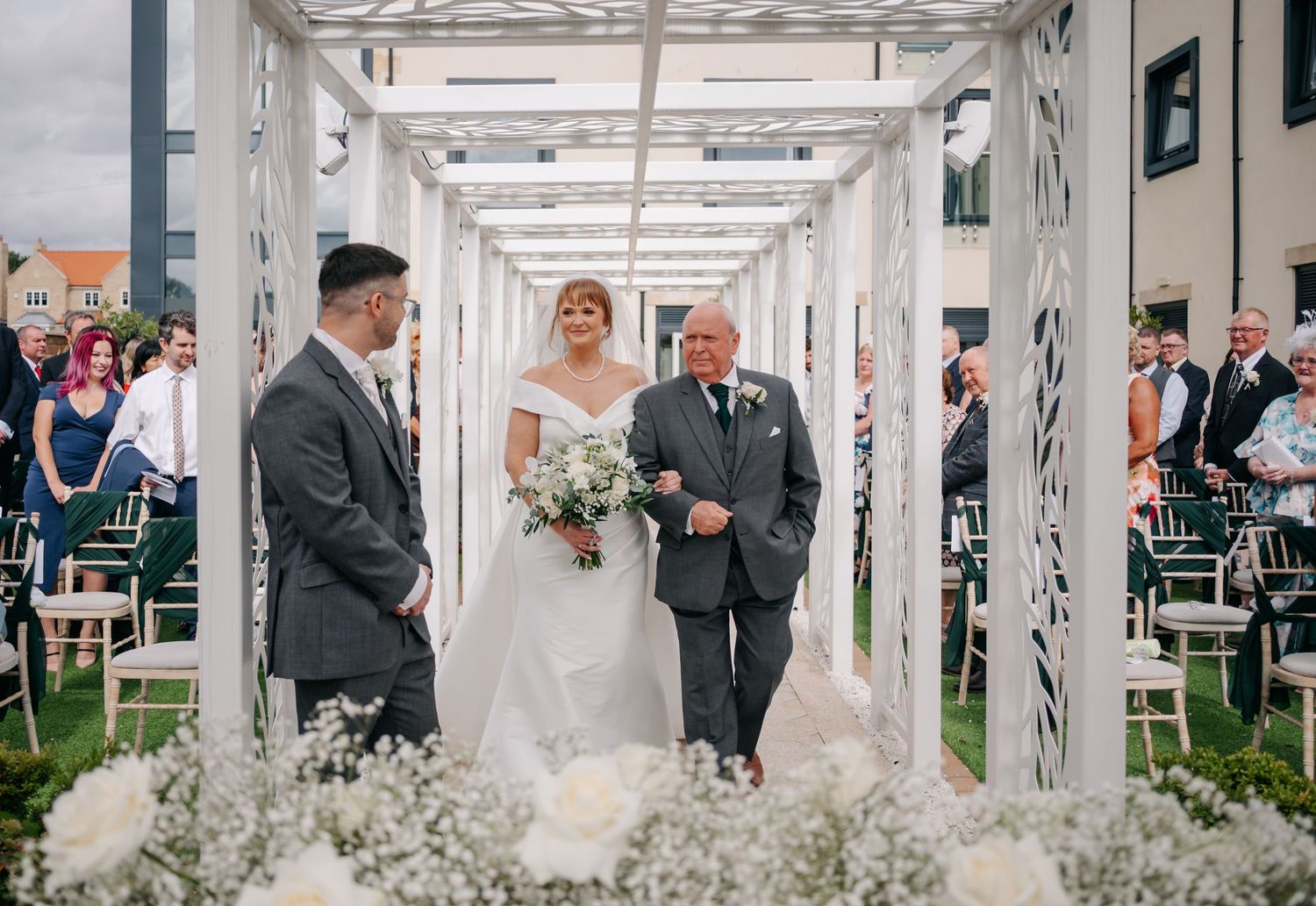 A white pergola decorated with floral arrangements for a wedding ceremony.