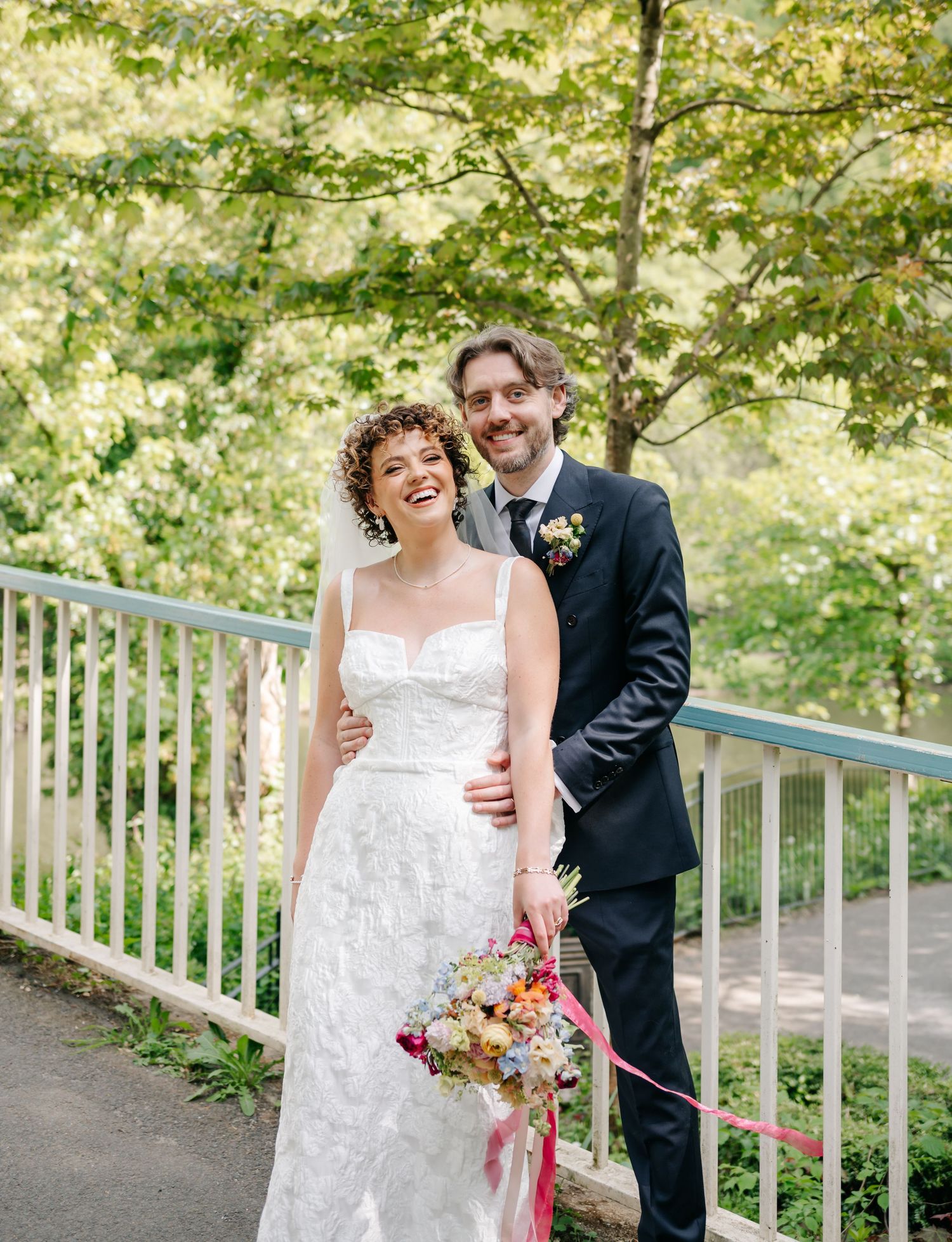 Newlyweds share a joyful moment on a garden path with white railings.