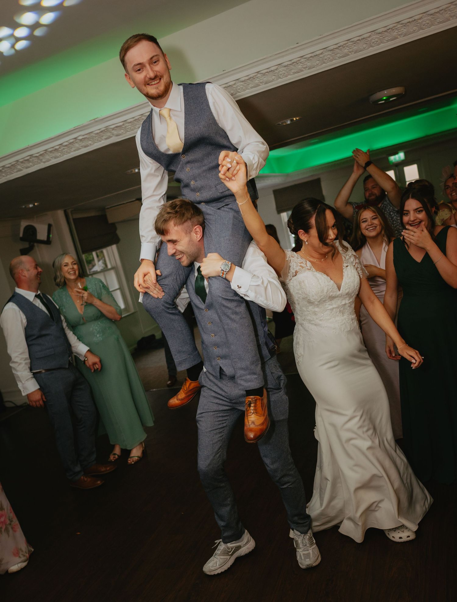 Wedding reception dance floor filled with energetic celebration and green lighting.