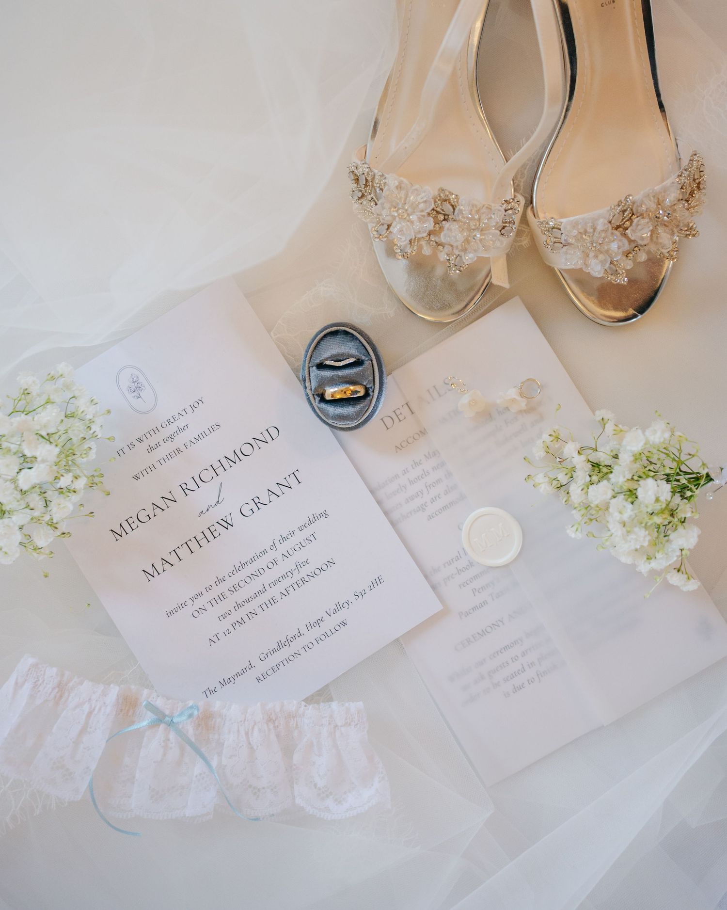 Wedding invitation and bridal shoes with delicate floral details alongside wedding rings and a white garter.