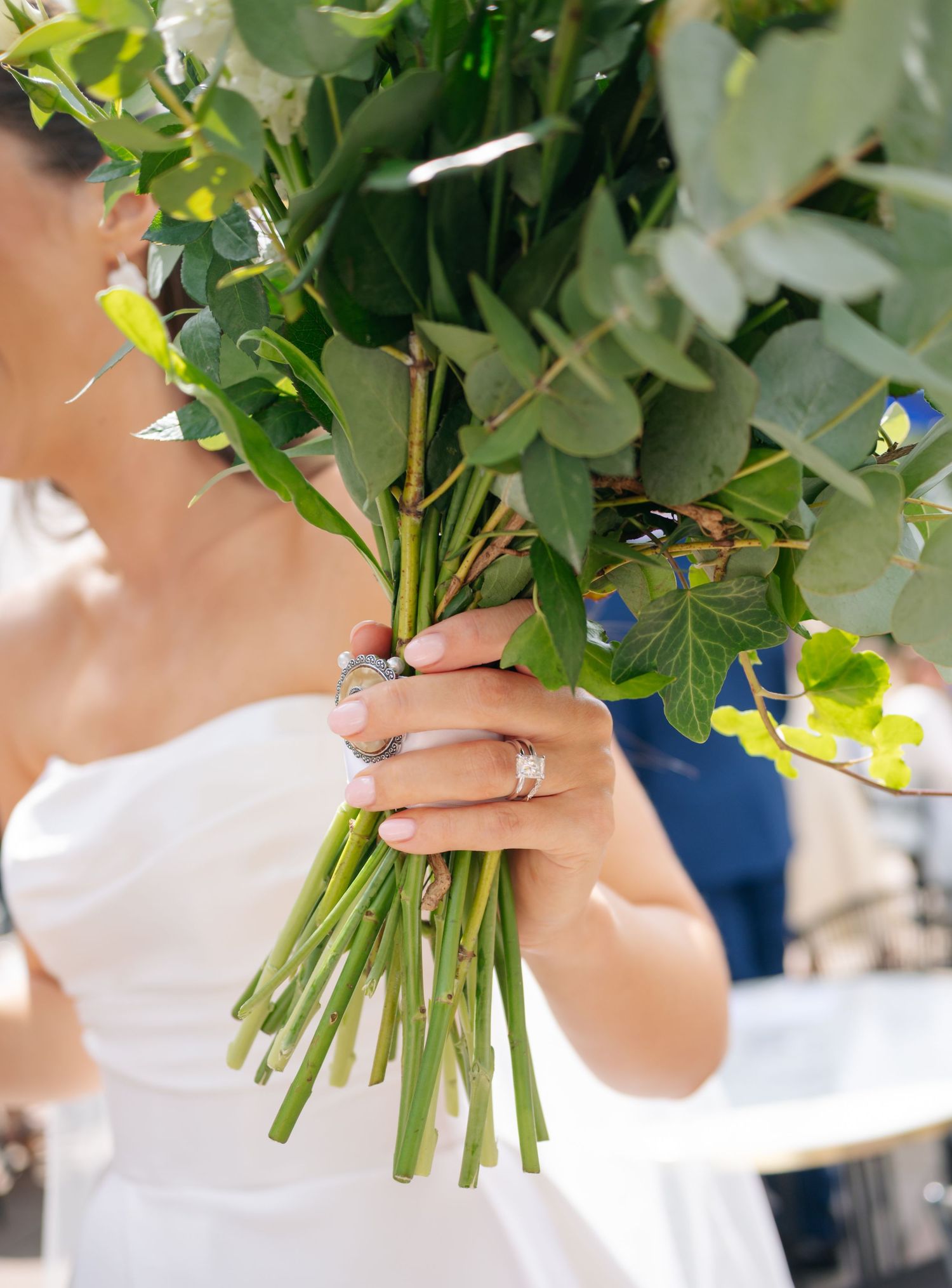 Close-up detail of hands holding a fresh green and white wedding bouquet with stems.