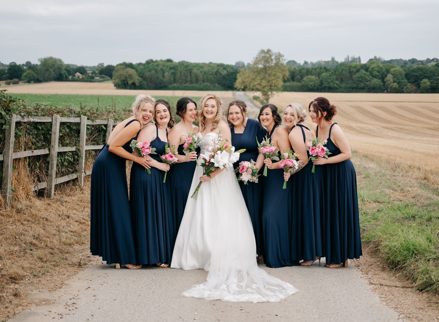 Bridesmaids in navy blue dresses pose together outdoors on a rural dirt path.