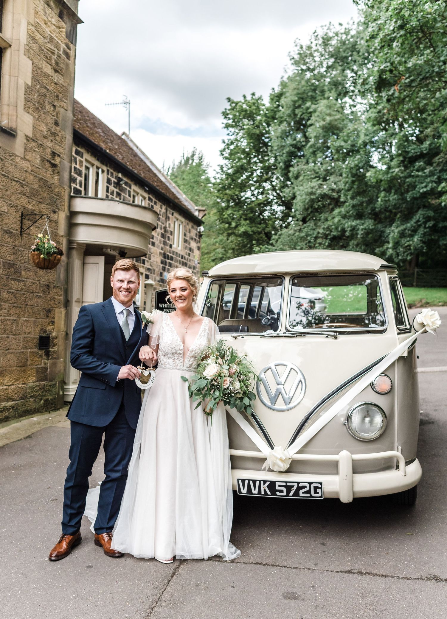 A vintage white VW bus parked outside a stone building during a wedding.