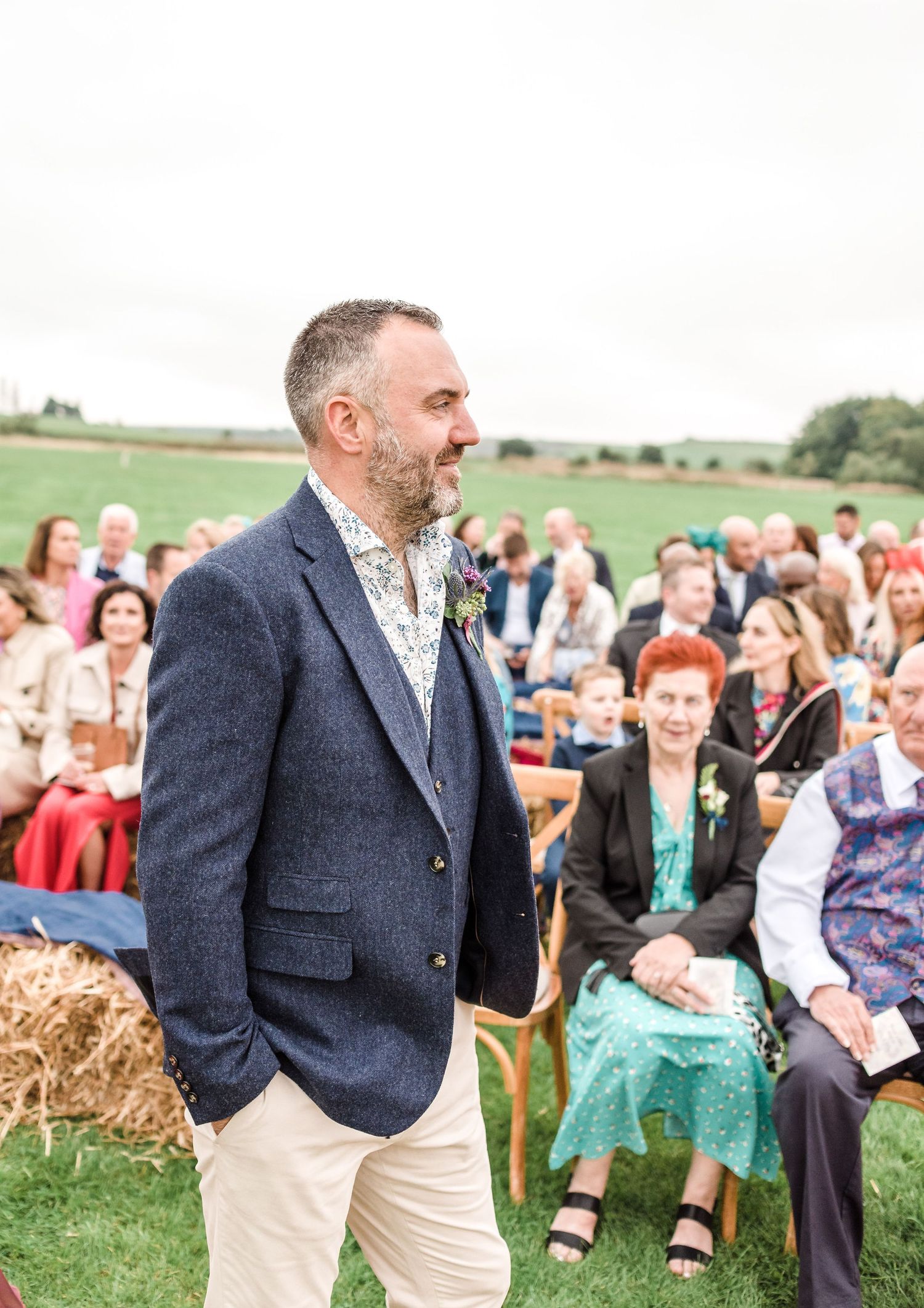 Speaker addressing seated guests at an outdoor ceremony with hay bales for seating.