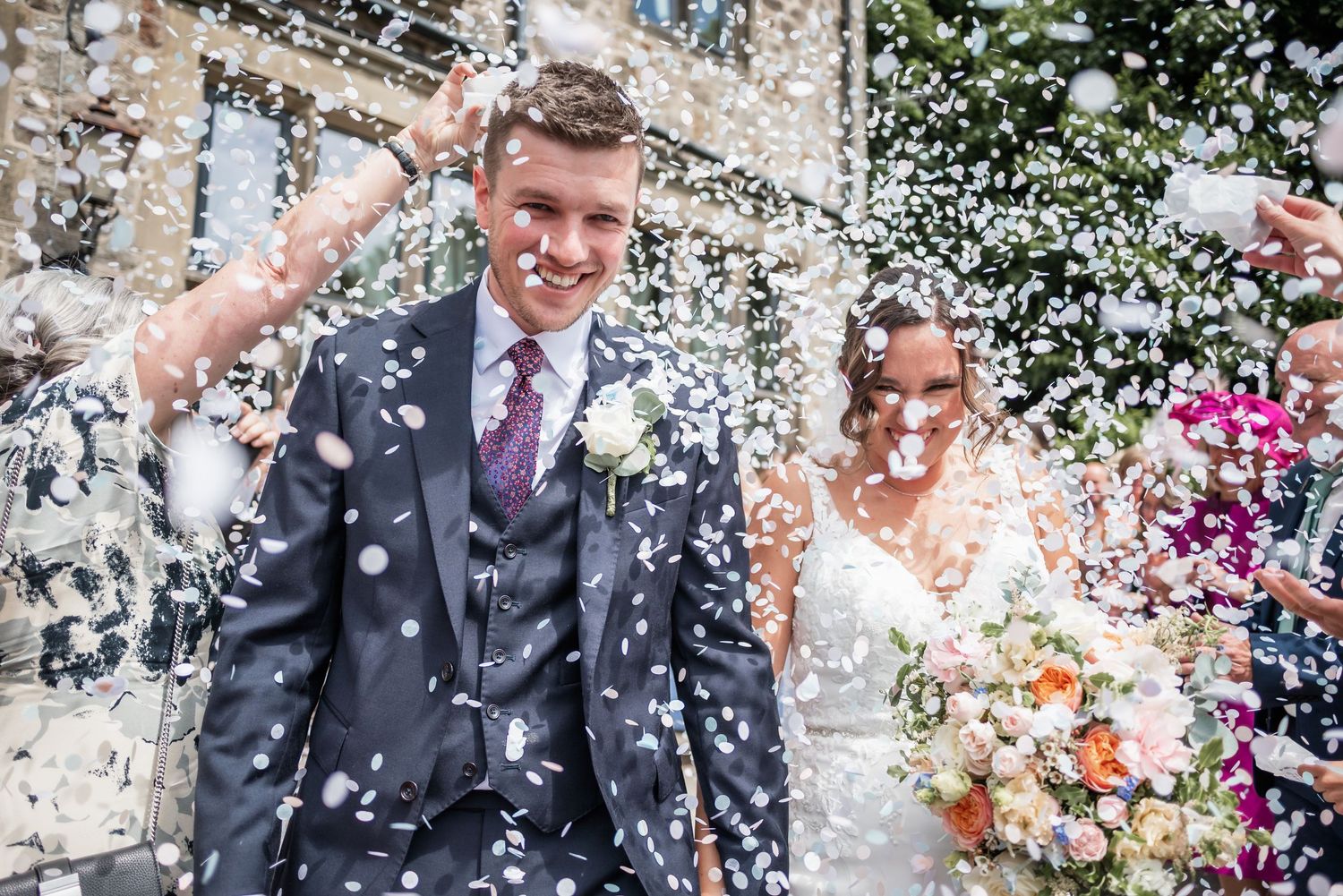 Joyful wedding couple celebrates amidst shower of white confetti outdoors.
