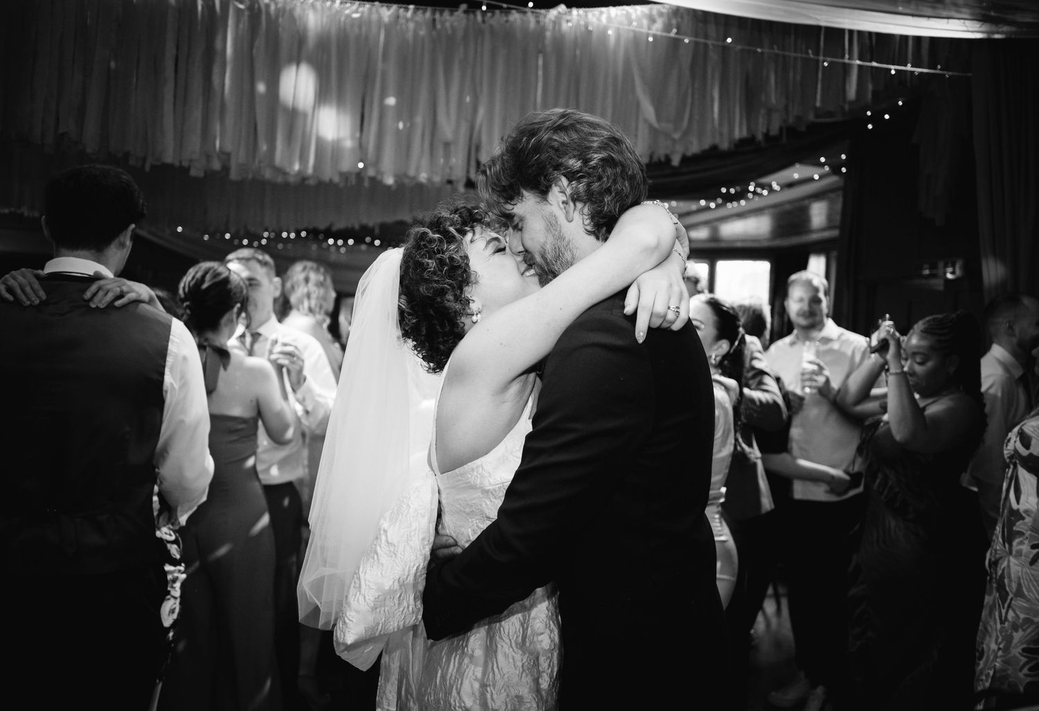 Black and white photo captures romantic dance moment under twinkling lights.