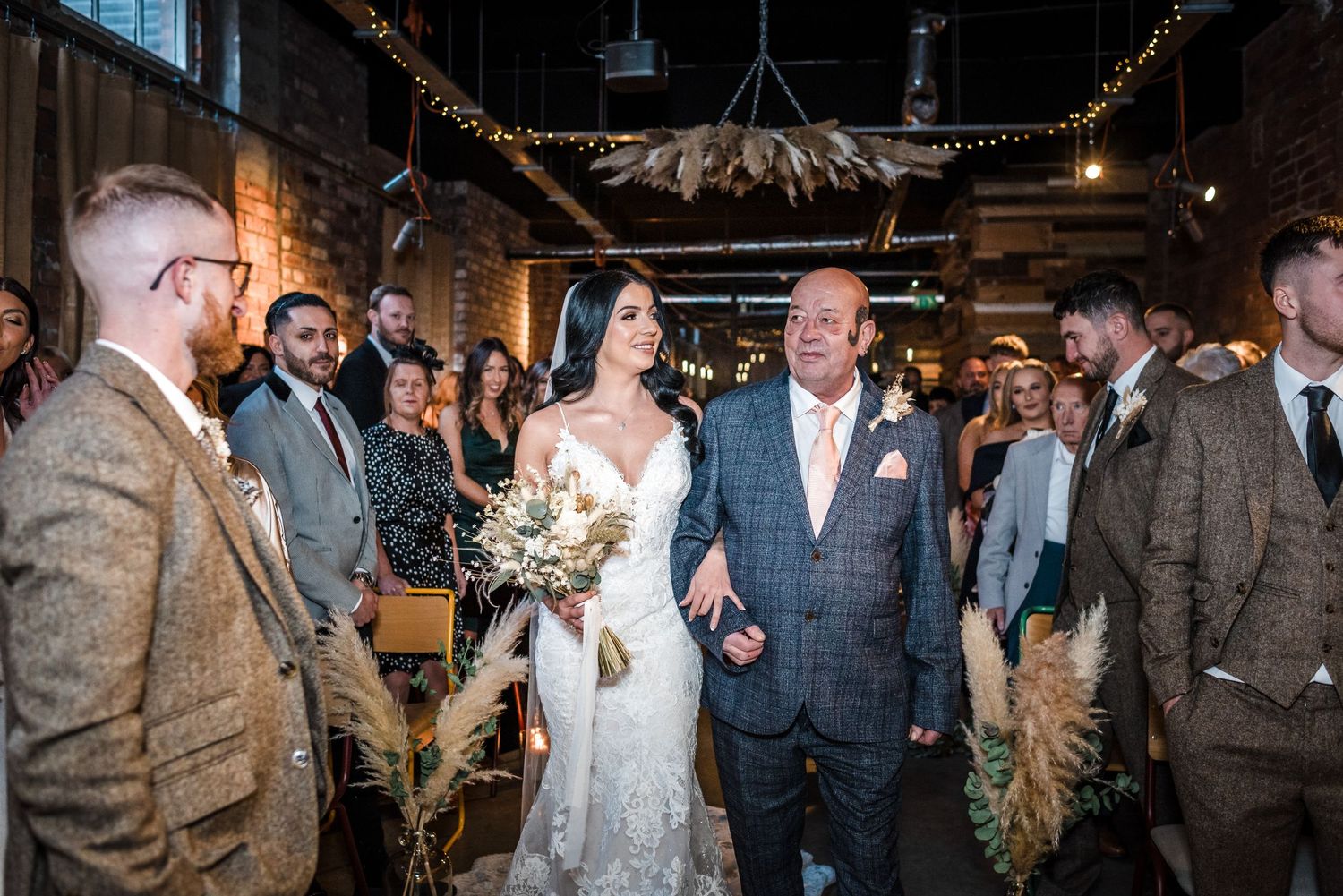 Newlyweds walking down the aisle at an industrial-style venue with string lights overhead.