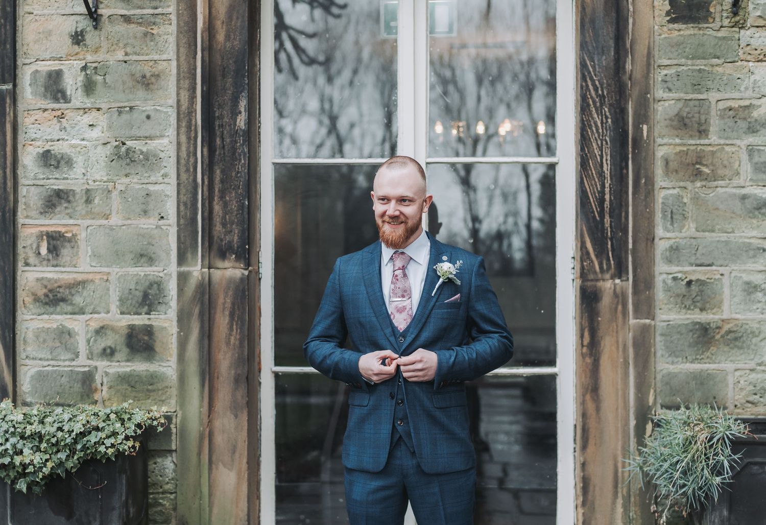 A suited figure poses confidently against rustic stone architecture.