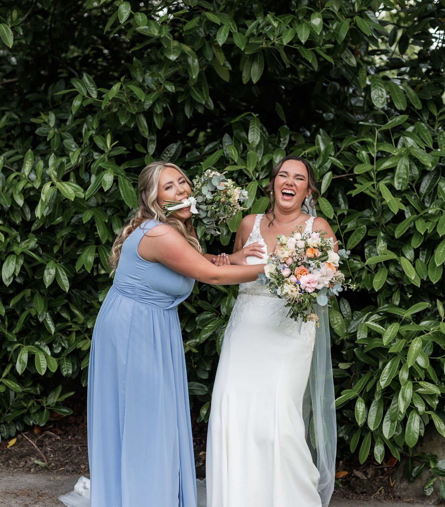 Candid moment of laughter between wedding party members against green foliage backdrop.