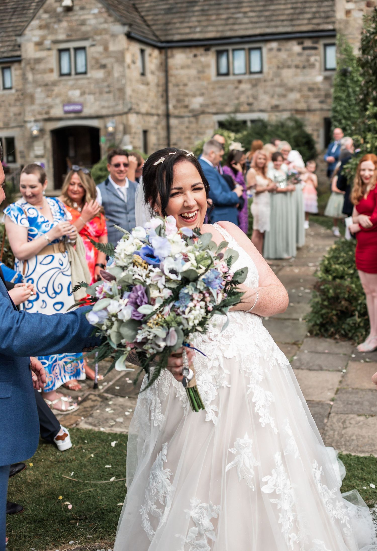 Joyful wedding celebration outside stone building with confetti and happy reactions.