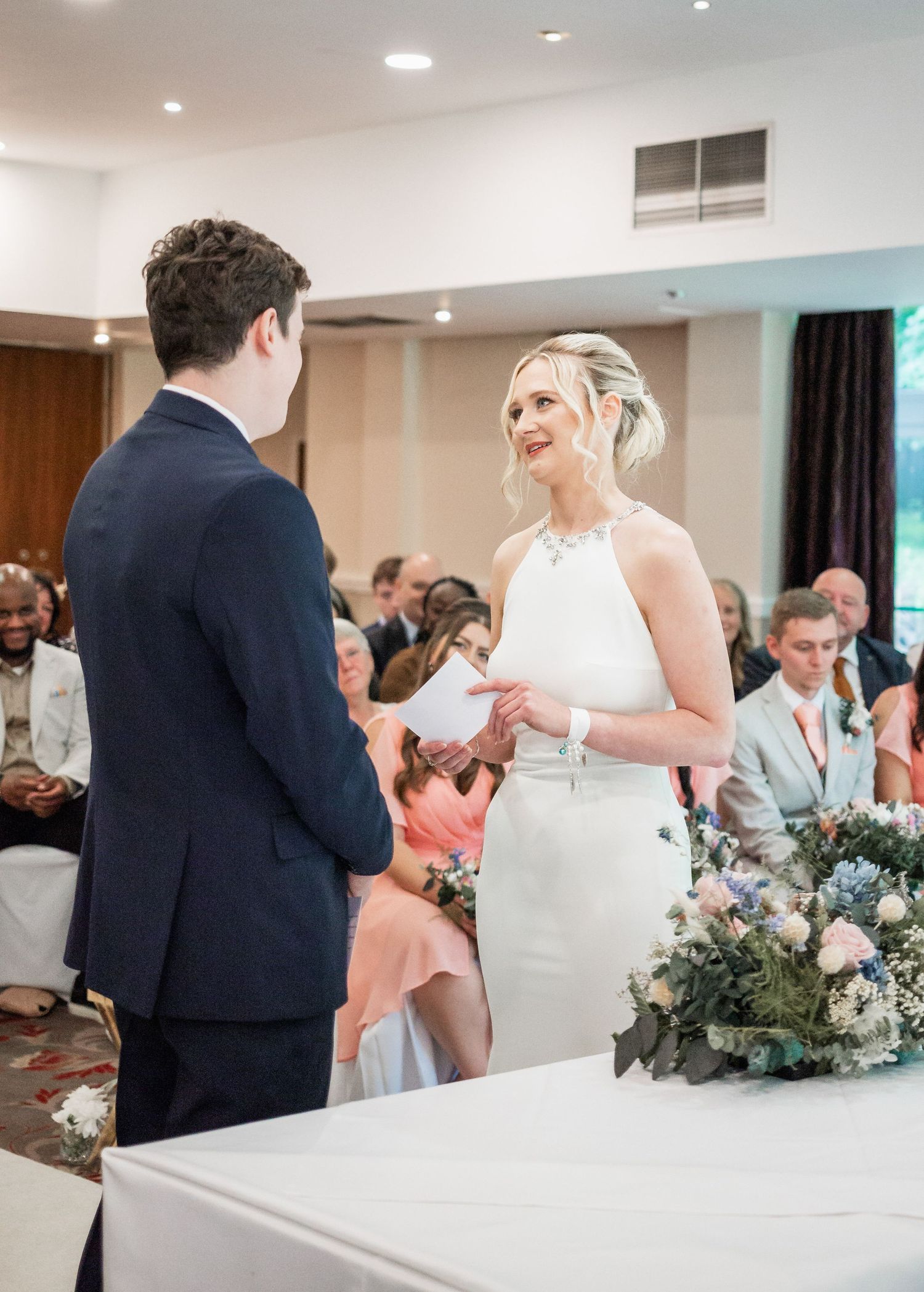 Wedding ceremony exchange at modern indoor venue with floral arrangements and seated guests.
