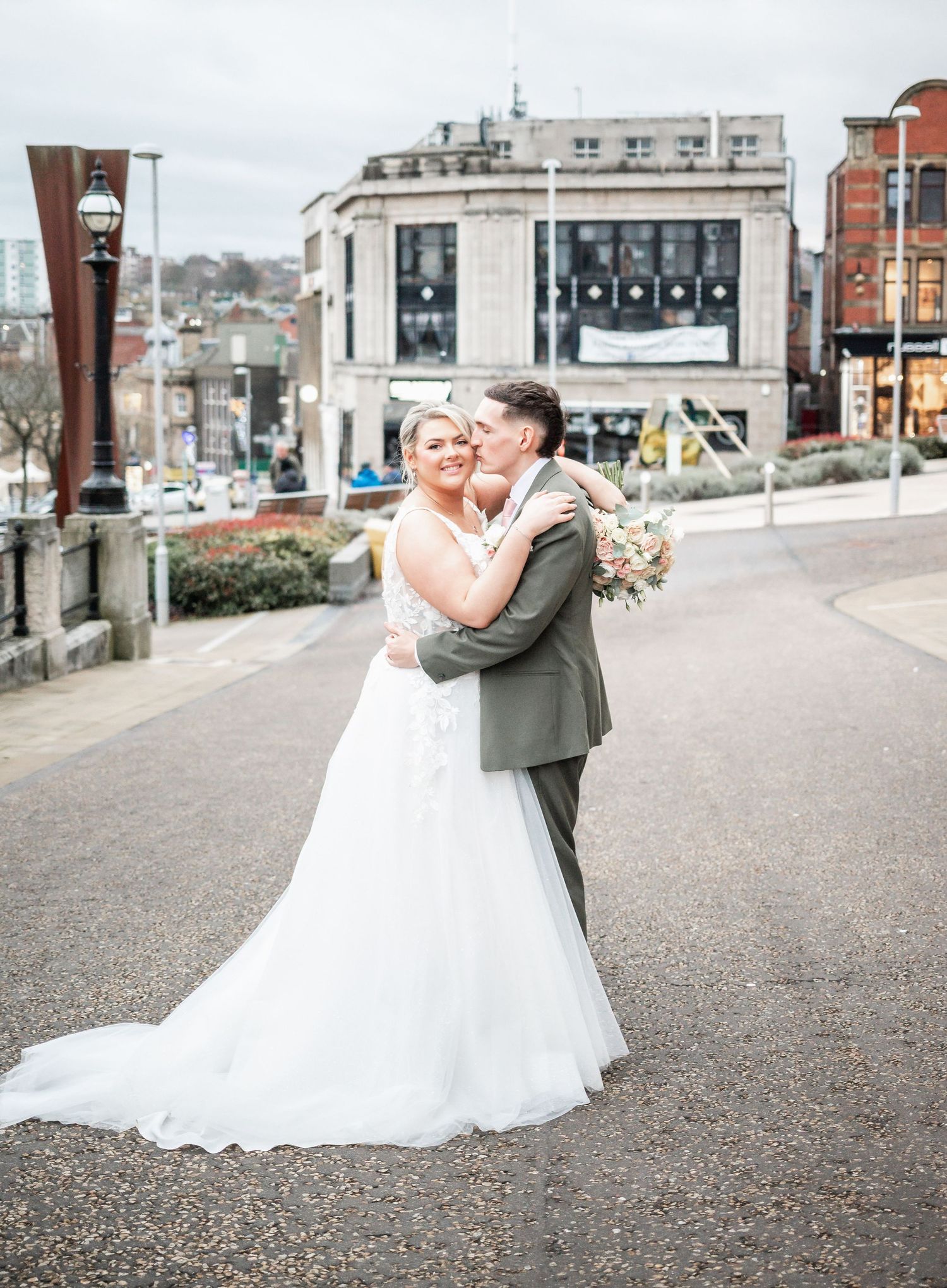 A romantic wedding moment captured on a city street with classic architecture in the background.