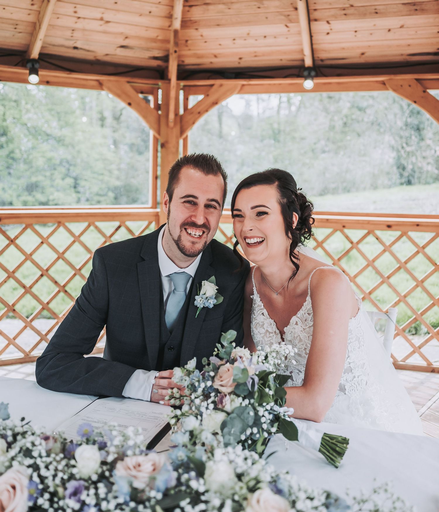A happy couple shares a moment together under a wooden gazebo with floral decorations during their wedding ceremony.