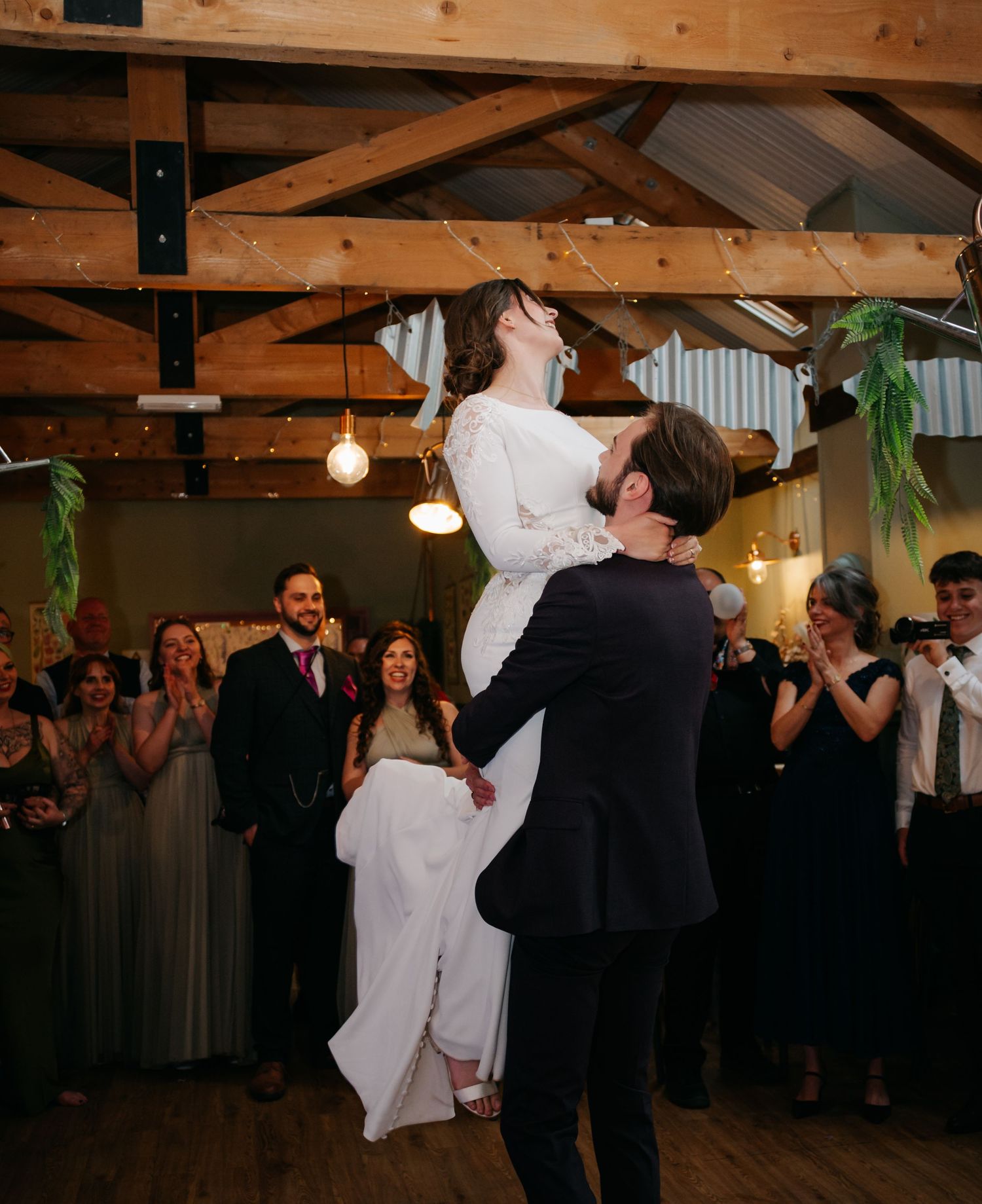 Wedding reception first dance in a rustic wooden barn venue with hanging lights.