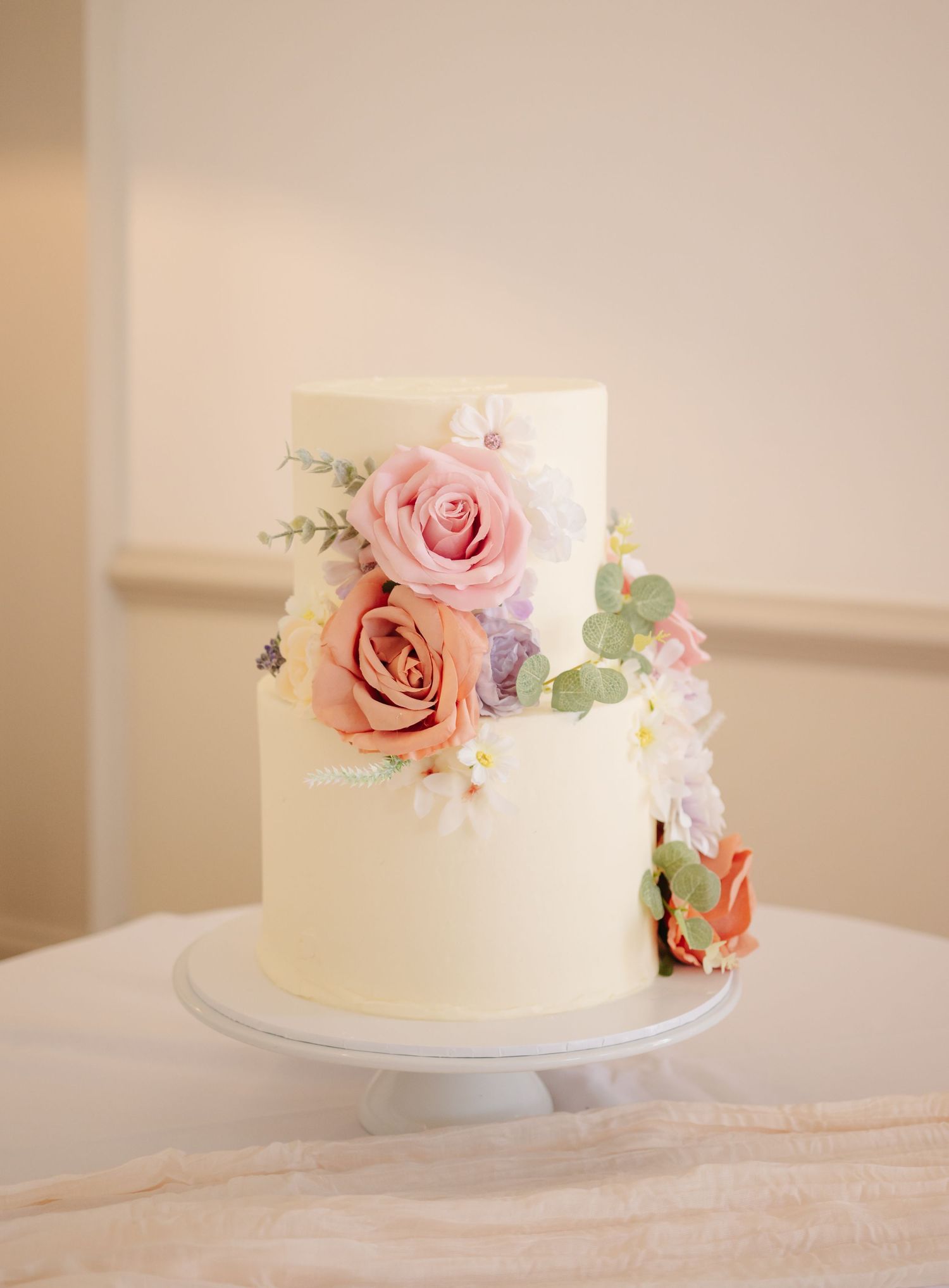 Elegant white wedding cake decorated with delicate pink roses and eucalyptus on a simple cake stand.