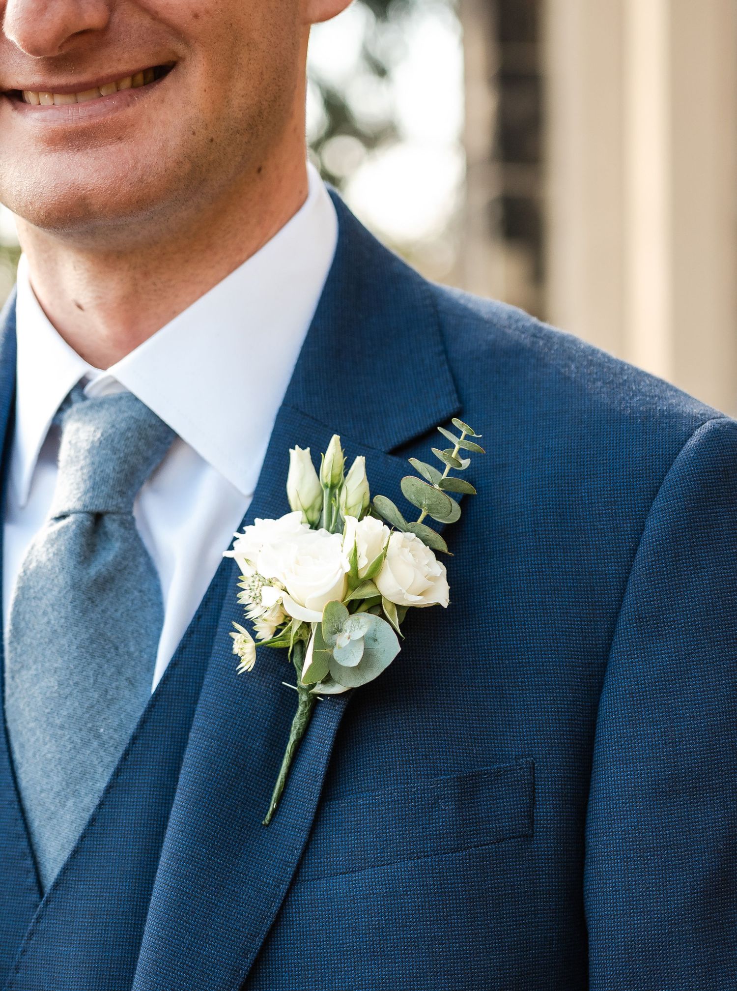 Groomsmen in navy blue suits with gray ties and white boutonnieres stand together at a formal wedding.