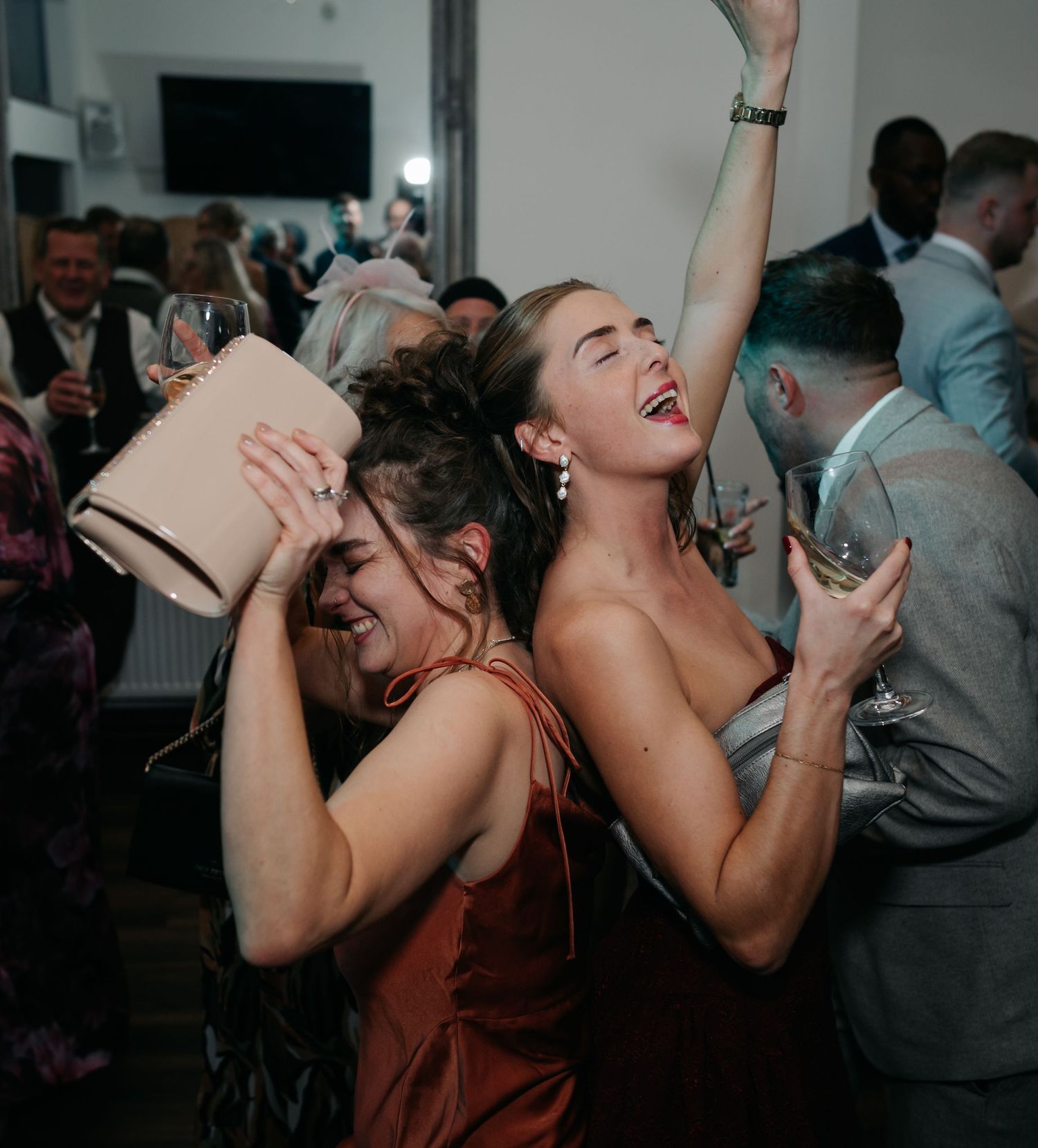 Wedding party members laughing and dancing energetically at a dimly lit indoor reception.