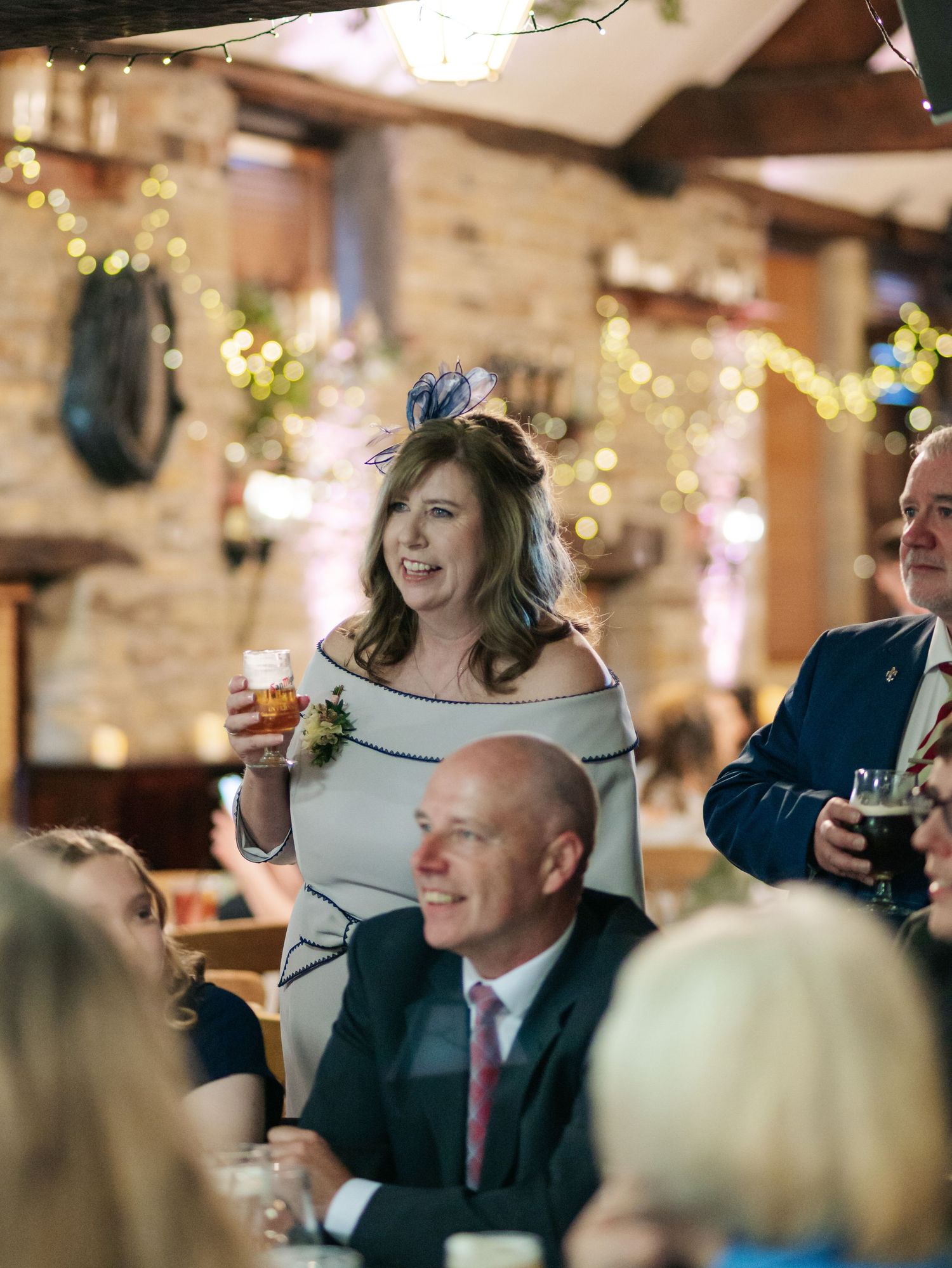 Wedding reception guests enjoying drinks and conversation under warm lighting in a rustic venue.