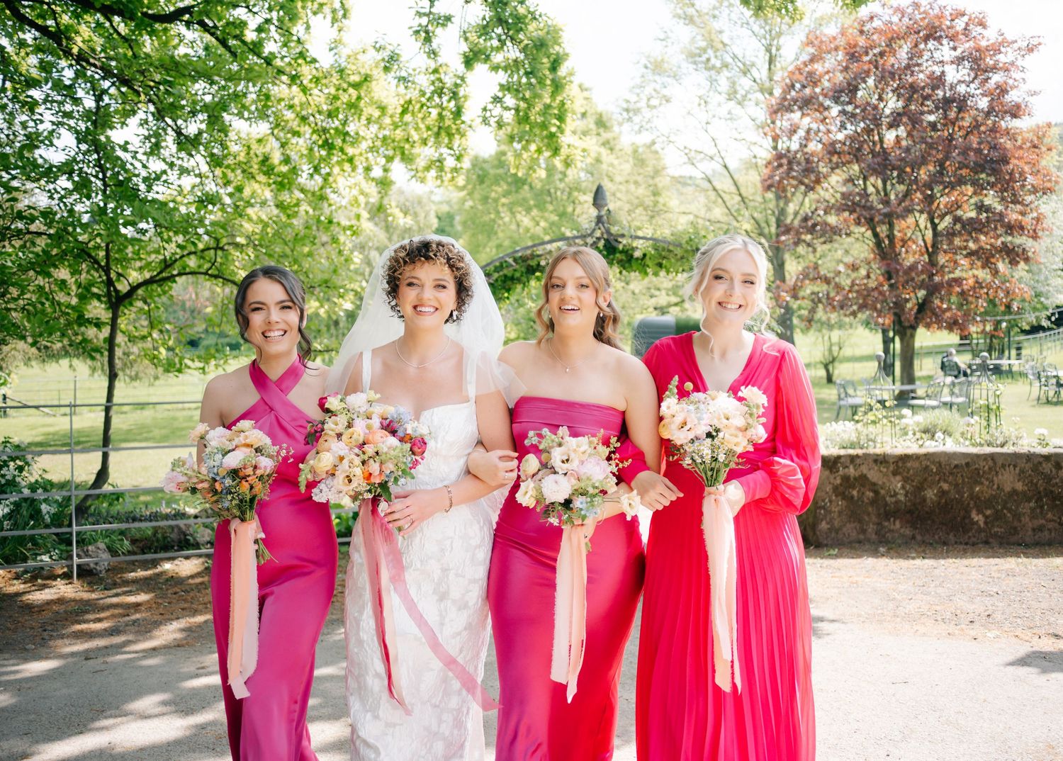 Wedding party members in vibrant pink dresses stand together outdoors for formal photos.