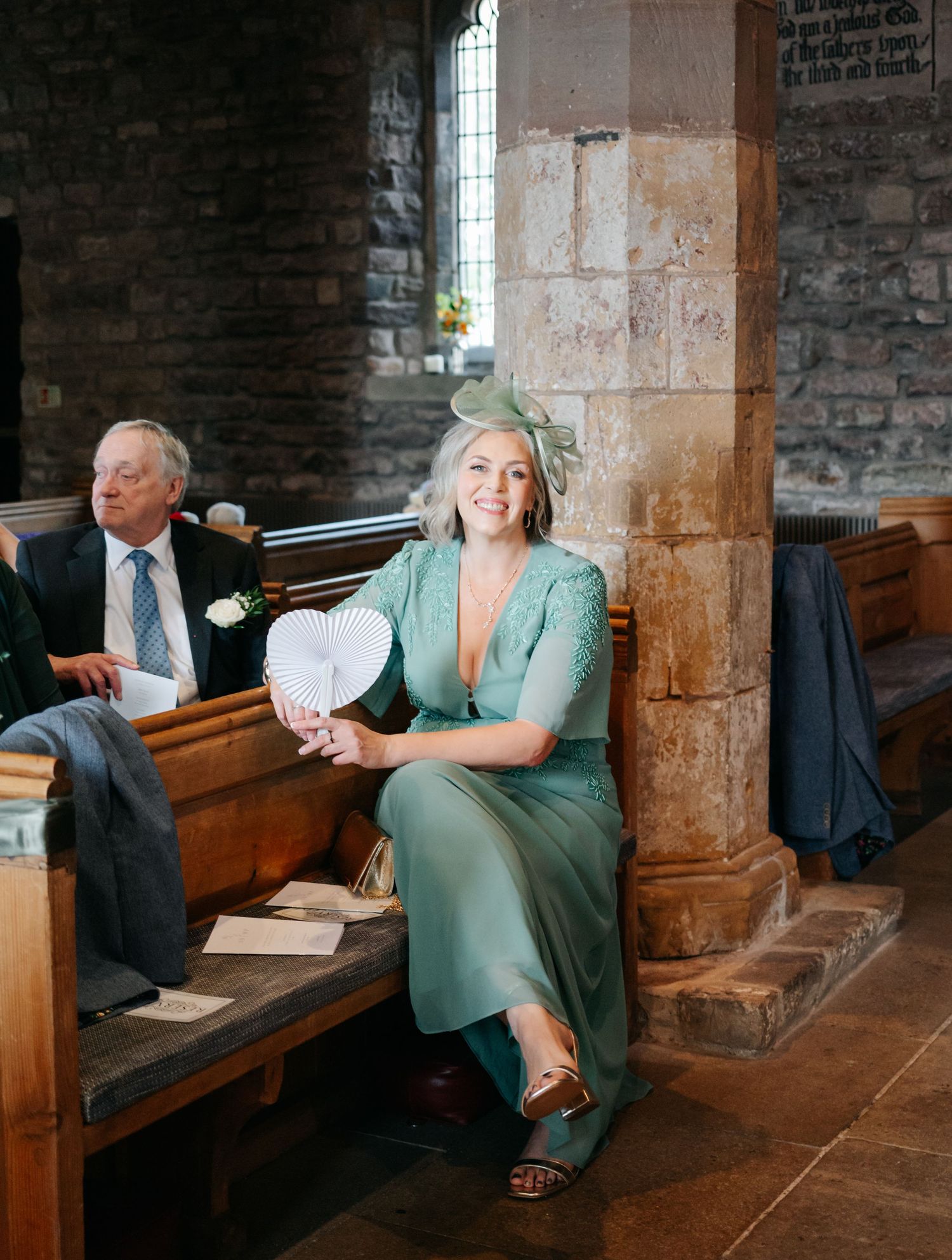Wedding guests relax on wooden church pews in a historic stone chapel with natural lighting.
