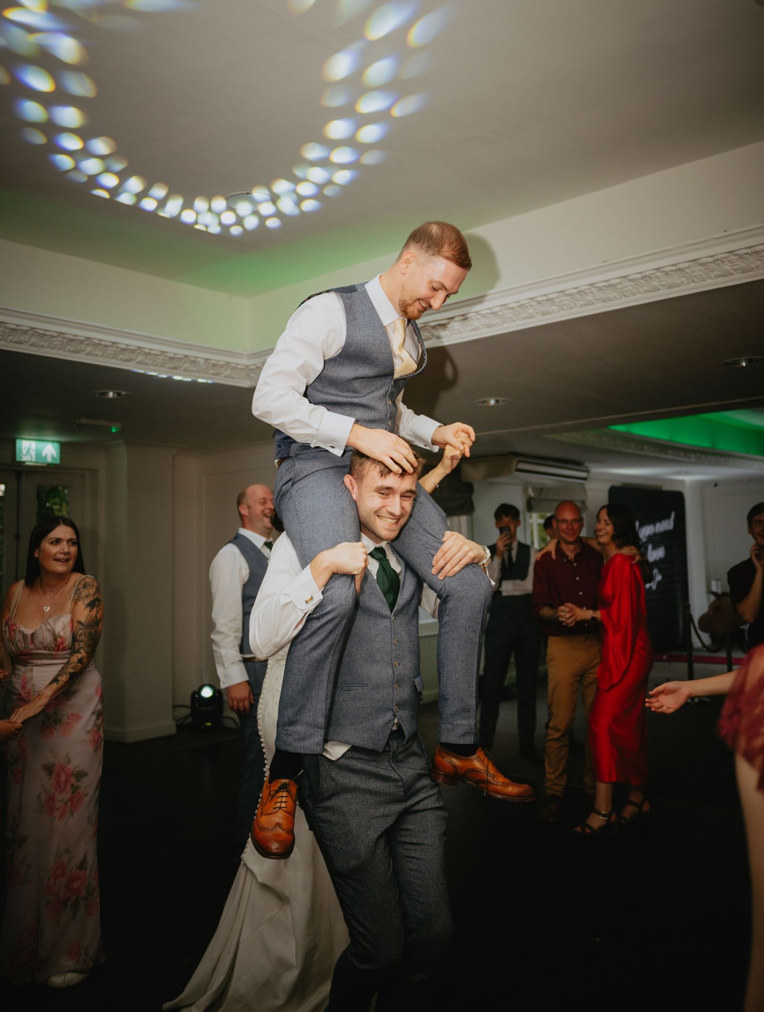 Wedding reception dance floor with party guests enjoying themselves under decorative lighting.
